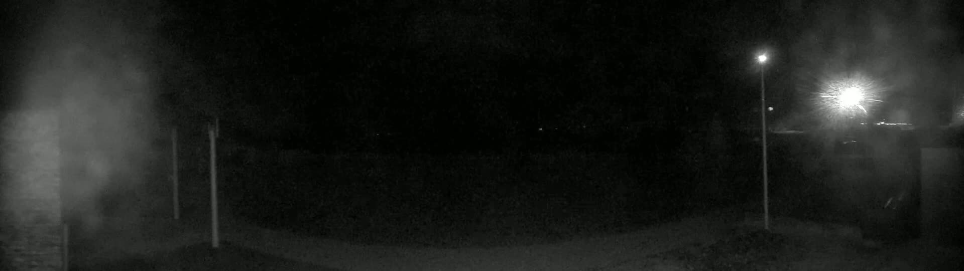 A nighttime, foggy scene shows two illuminated light posts and a dimly lit area beyond.