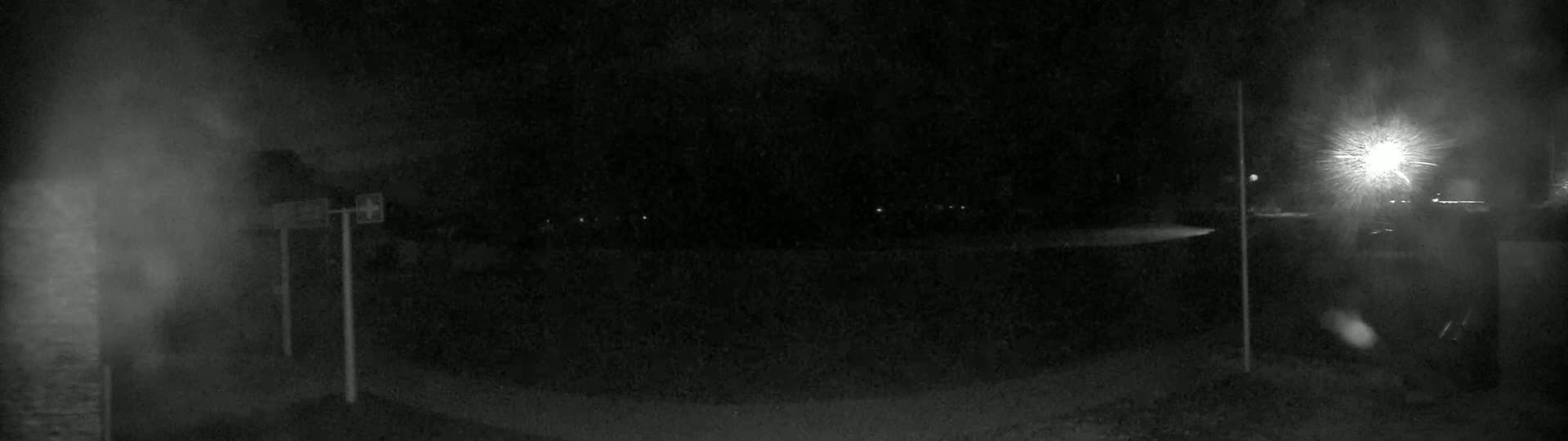 A nighttime, blurry view of a dark area with a bright light source in the upper right corner and faint lights in the distance.