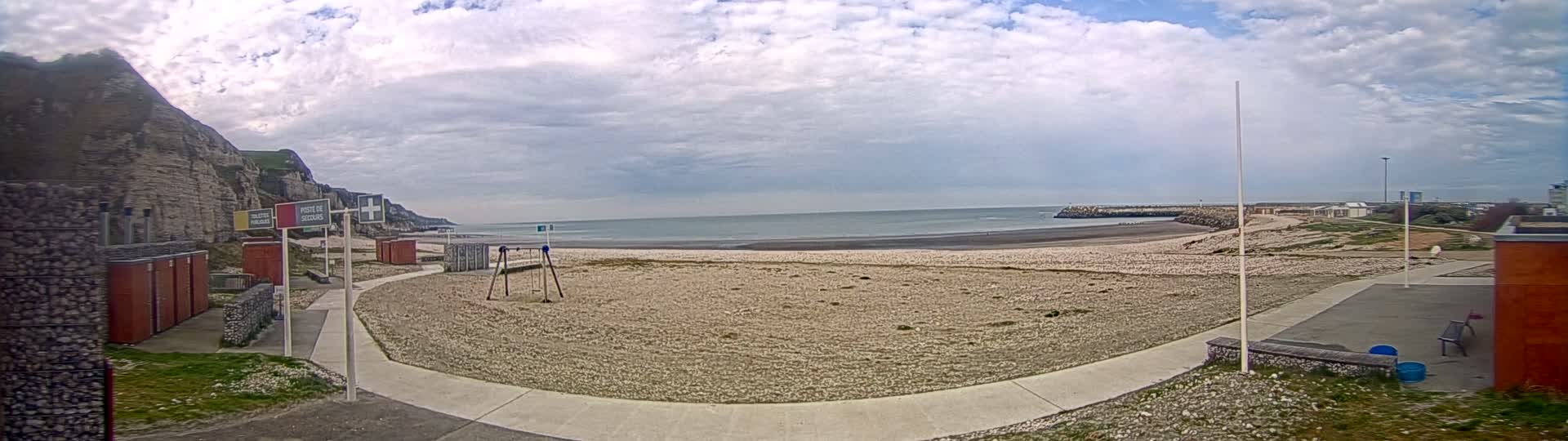 A mostly cloudy day at a beach with a sandy shore, a calm sea, and white cliffs in the background.