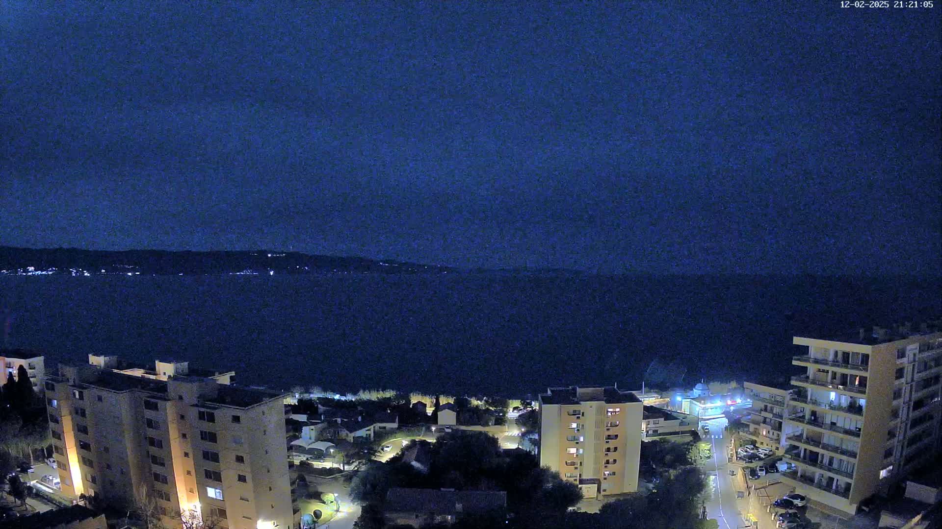 A nighttime view overlooking a dark body of water, with illuminated buildings and streets below a dark blue sky.