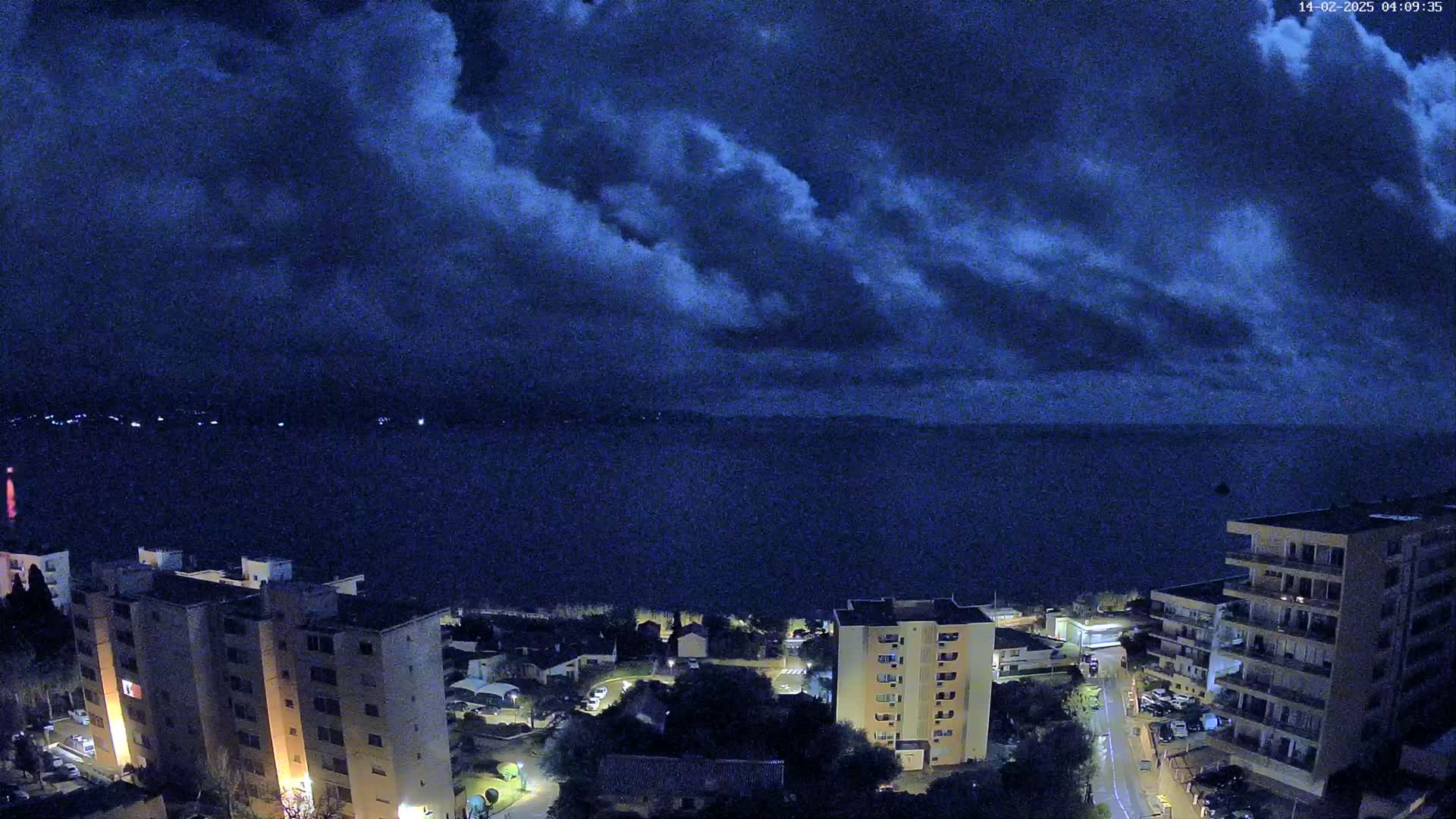 A nighttime view of apartment buildings near a dark body of water under a cloudy sky.