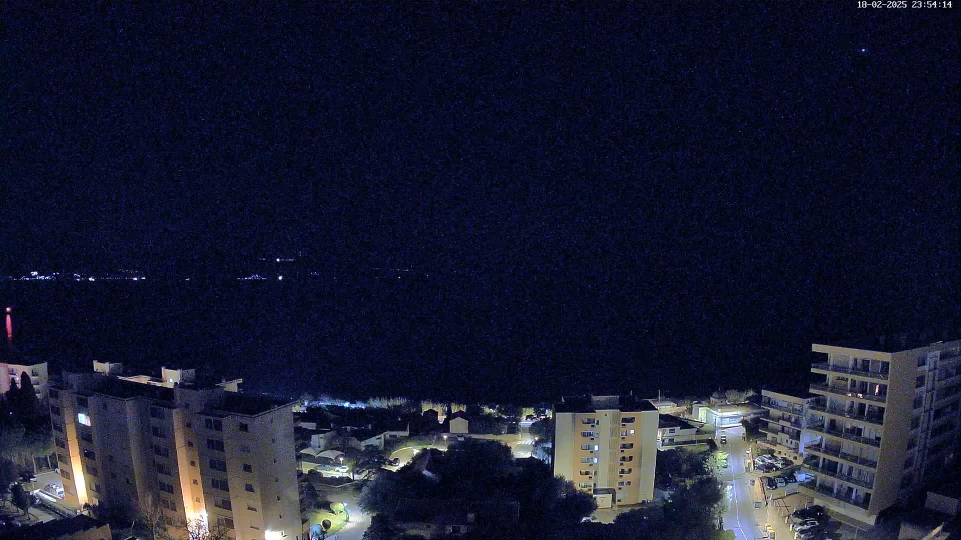 A nighttime aerial view of apartment buildings and a town, overlooking a dark body of water under a clear, starlit sky.