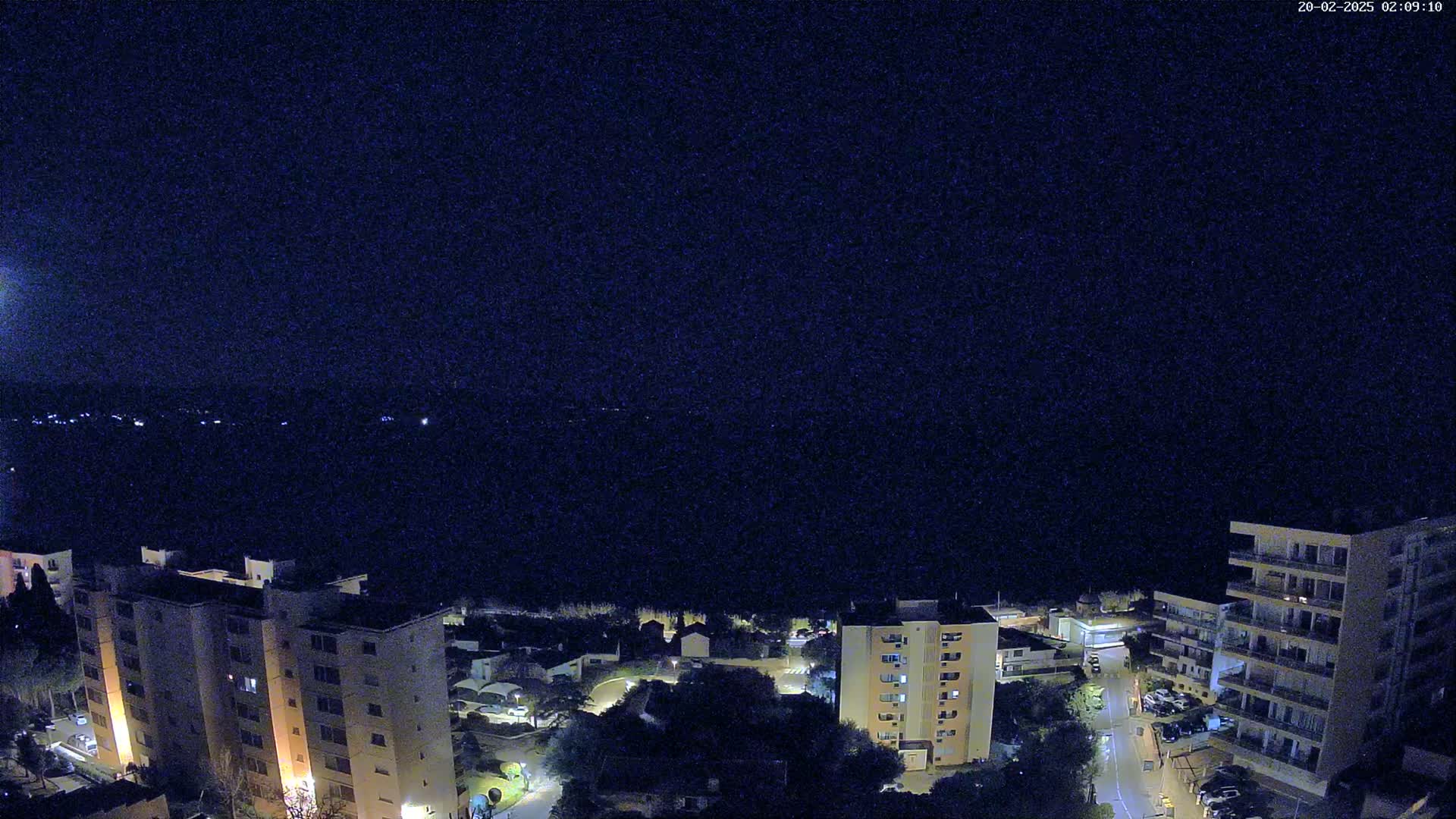A nighttime aerial view shows several apartment buildings illuminated against a dark, clear sky.