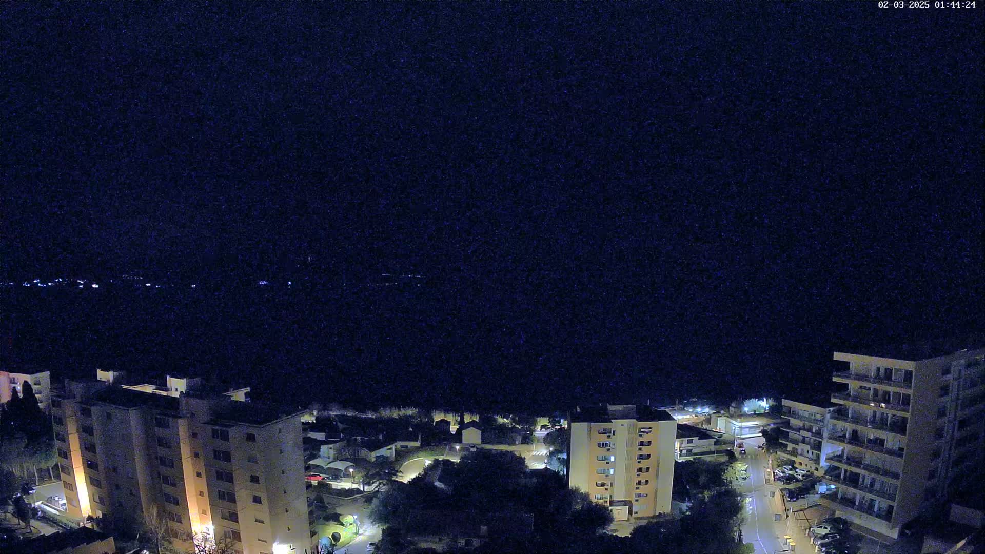 A nighttime aerial view shows several multi-story apartment buildings and surrounding streets in a residential area under a clear, dark sky.