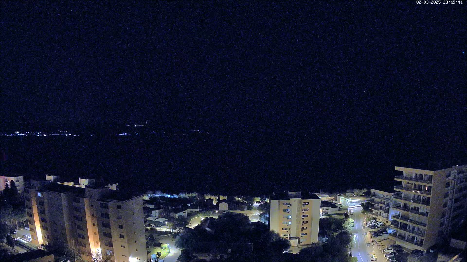 A nighttime, high-angle view shows a residential area with several multi-story buildings illuminated against a dark, clear sky.