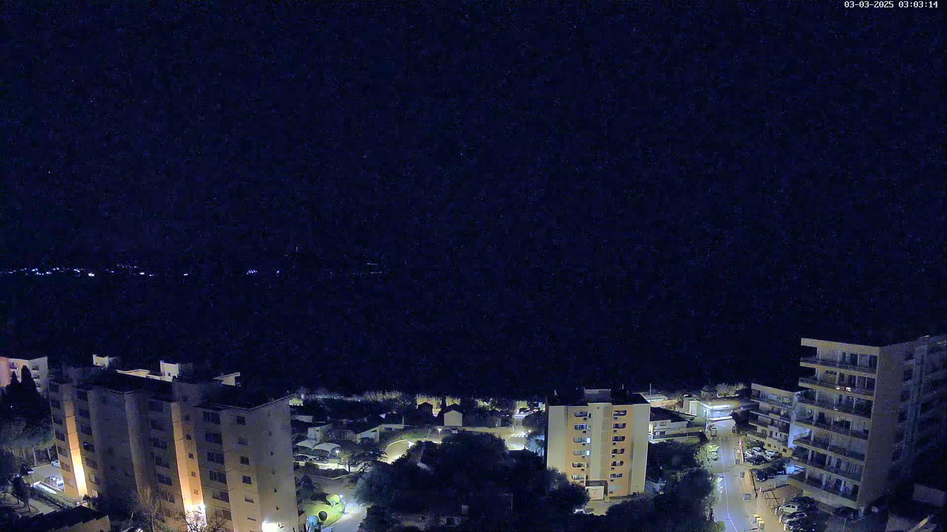 A nighttime aerial view shows several apartment buildings and a street, illuminated by lights, under a clear, dark sky.