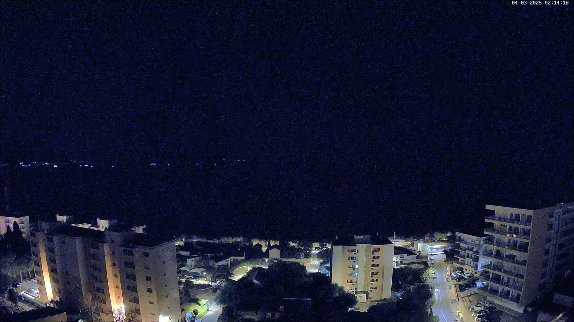 A nighttime aerial view shows several apartment buildings and surrounding streets and vegetation under a clear, dark sky.
