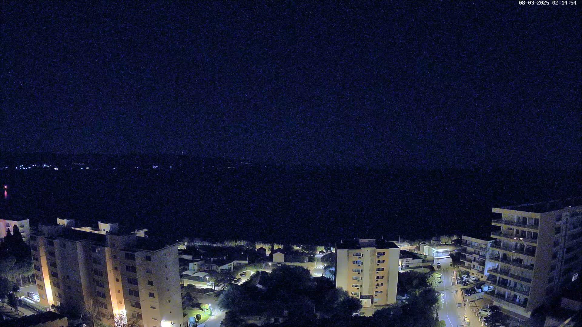 A nighttime aerial view shows several apartment buildings illuminated against a dark sky.