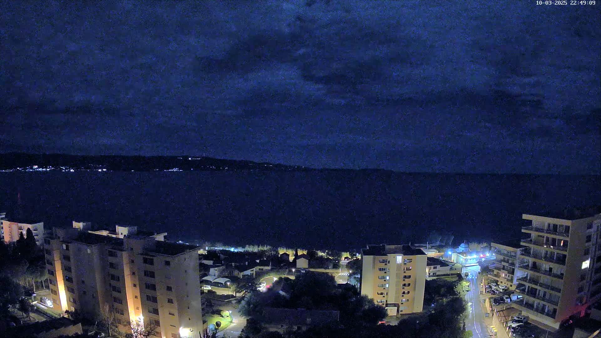 A nighttime view of a city beside a dark body of water under a cloudy sky.