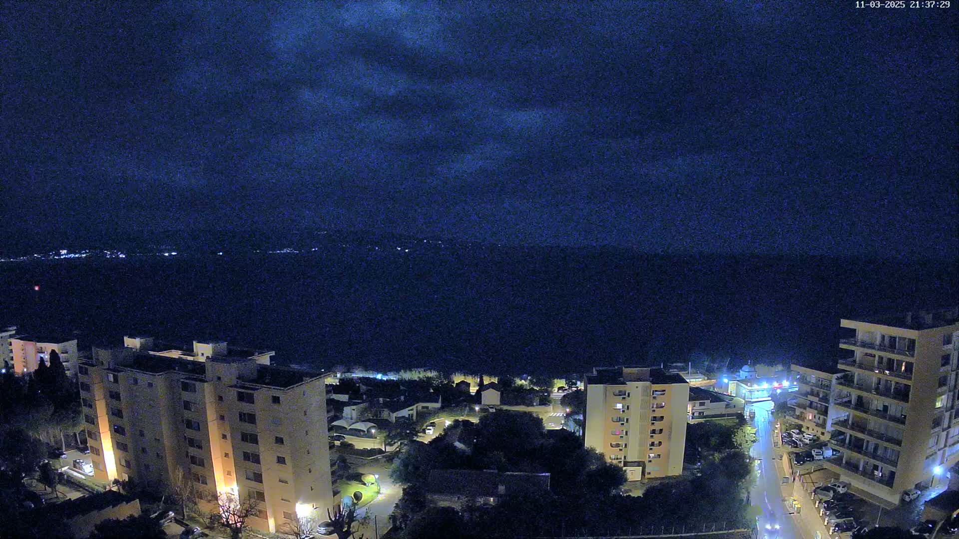 A nighttime view of a coastal town with several multi-story buildings under a dark, cloudy sky.