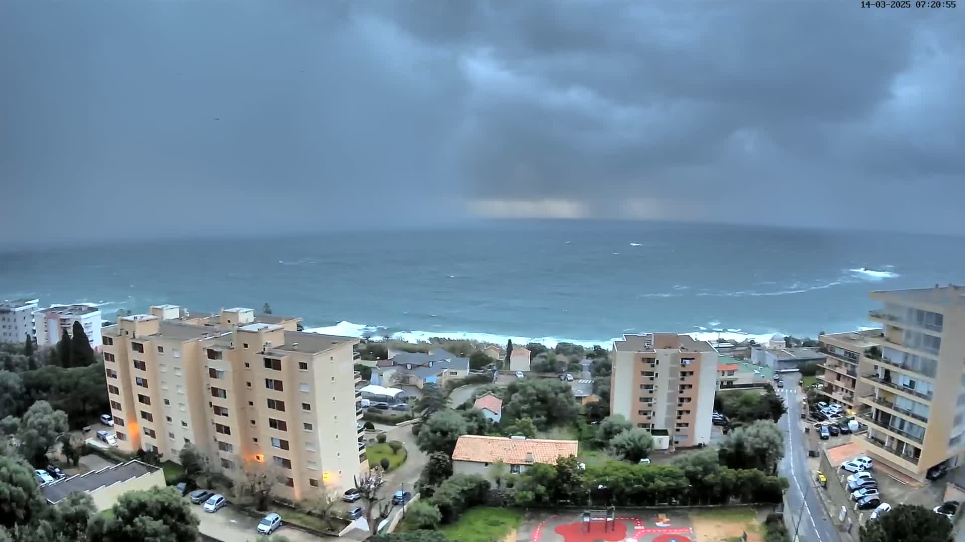 A coastal town with multi-story apartment buildings under a stormy, gray sky overlooking a choppy sea.