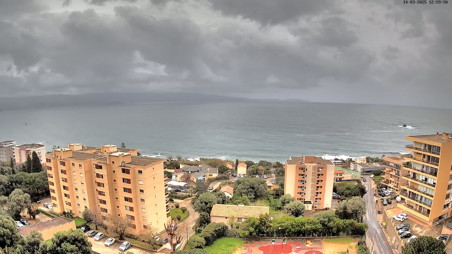 A coastal town overlooks a gray, wavy sea under a cloudy sky.