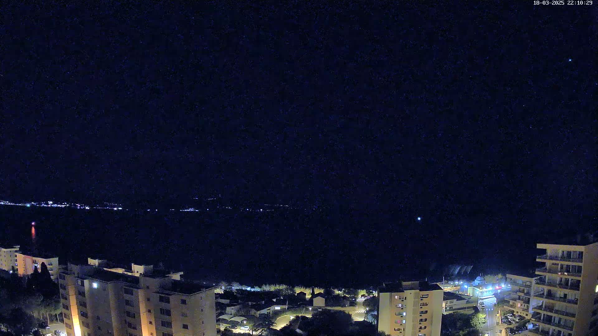 A nighttime view of a cityscape near a body of water under a clear, starry sky.
