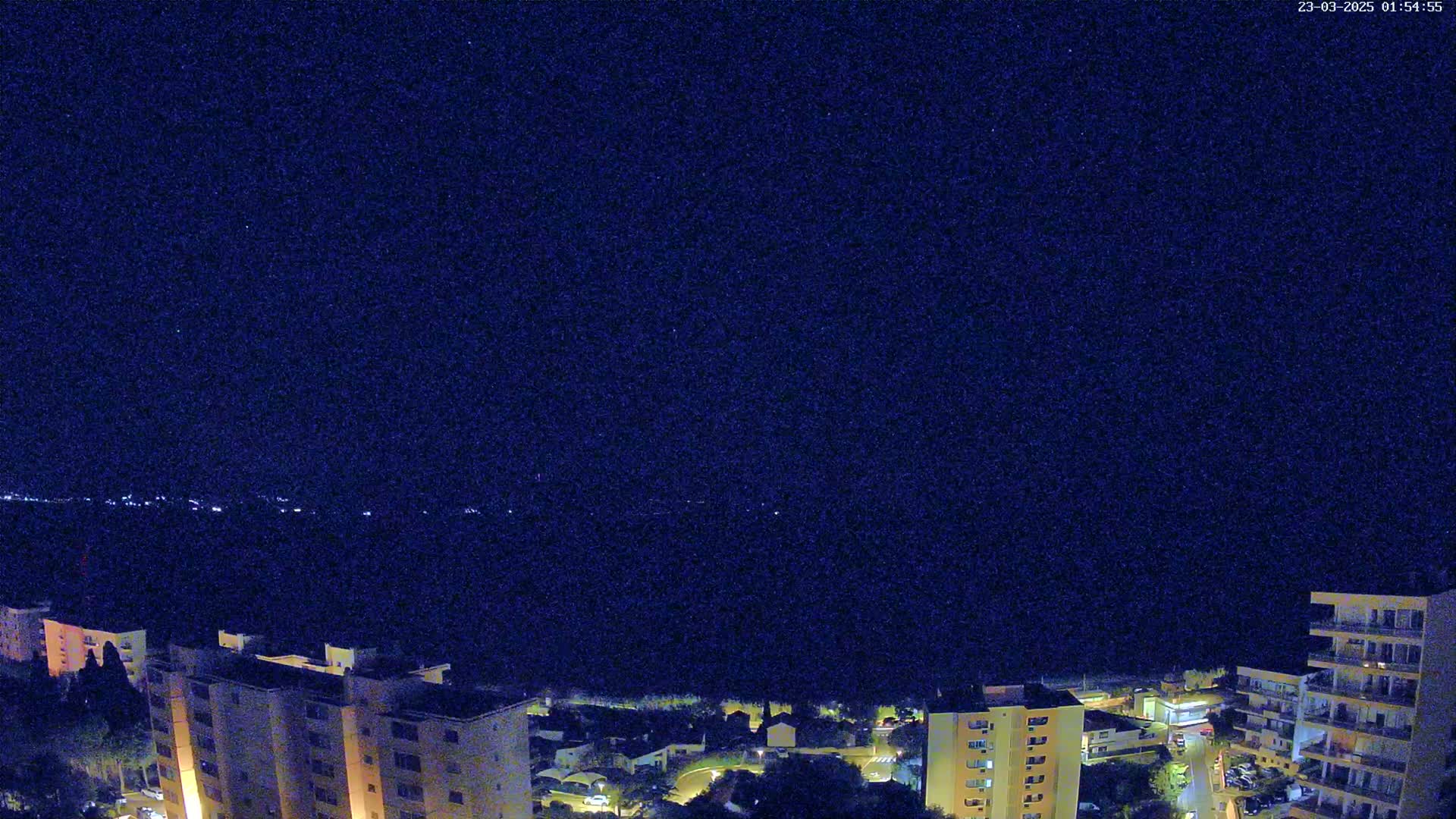 A nighttime aerial view of a town with apartment buildings, showing a clear, dark sky with stars.