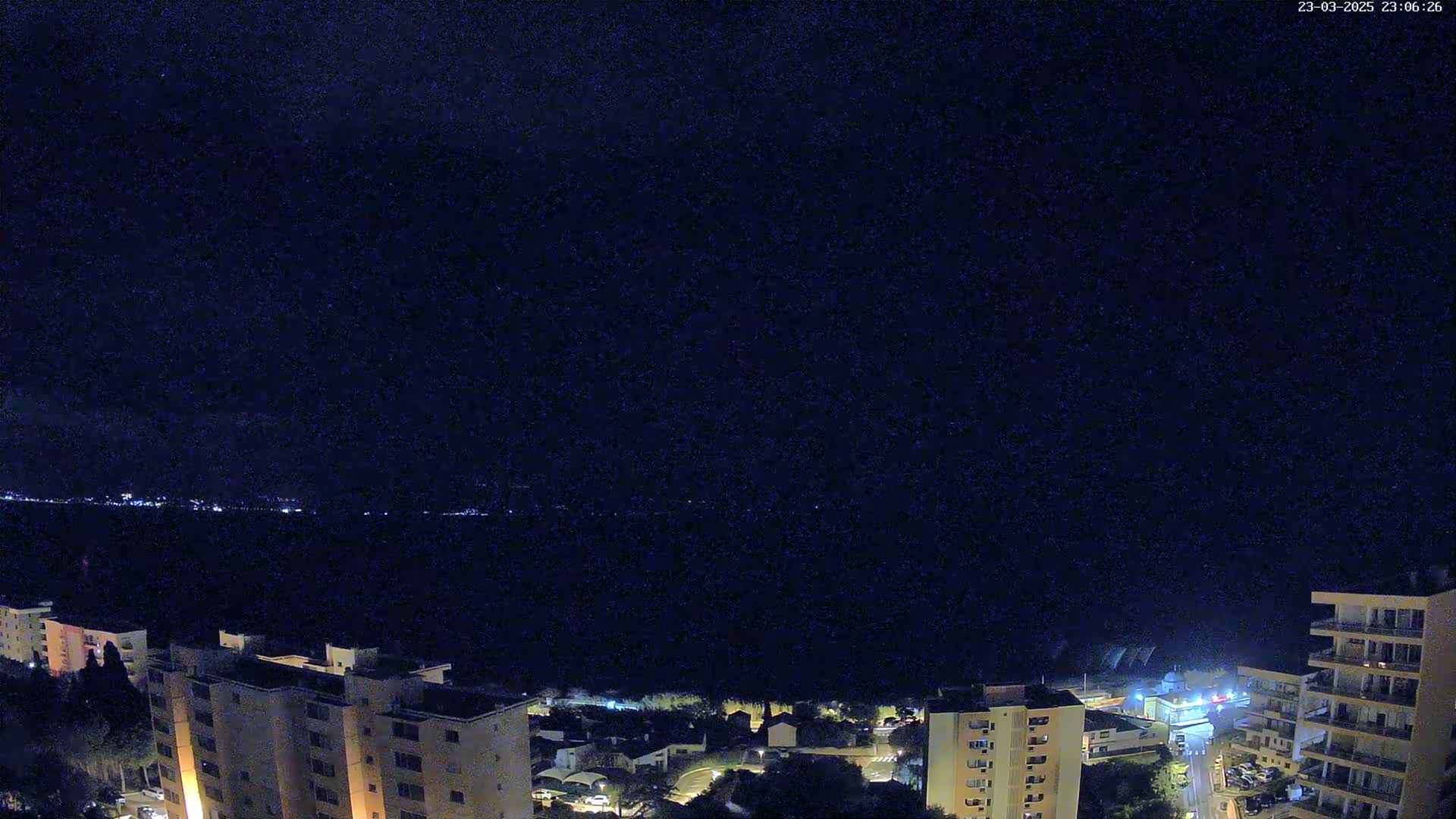 A nighttime view of a city overlooking a dark body of water under a clear, starlit sky.