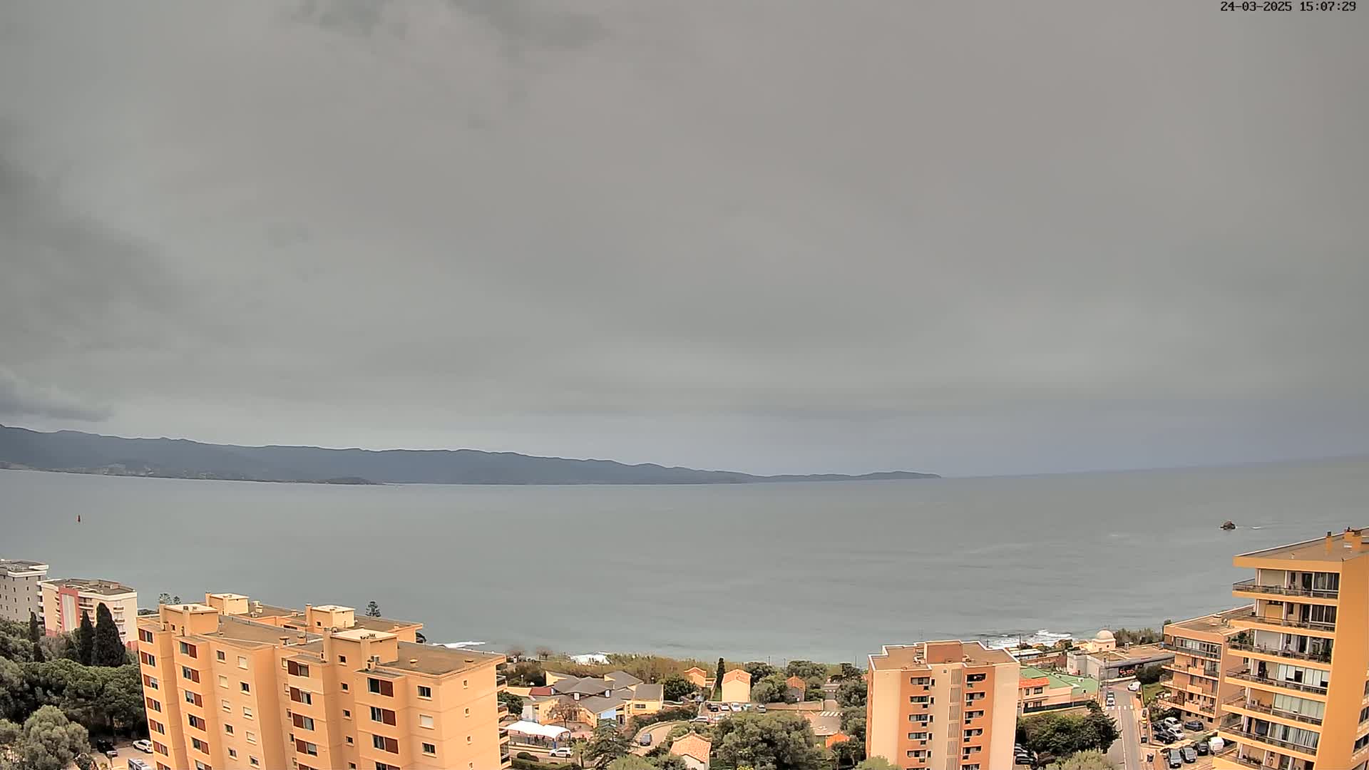 An overcast sky hangs over a calm sea, with apartment buildings and a coastline visible in the foreground.