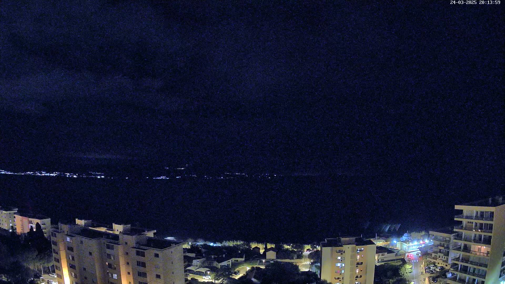 A nighttime view of a city near a body of water under a dark, cloudy sky.
