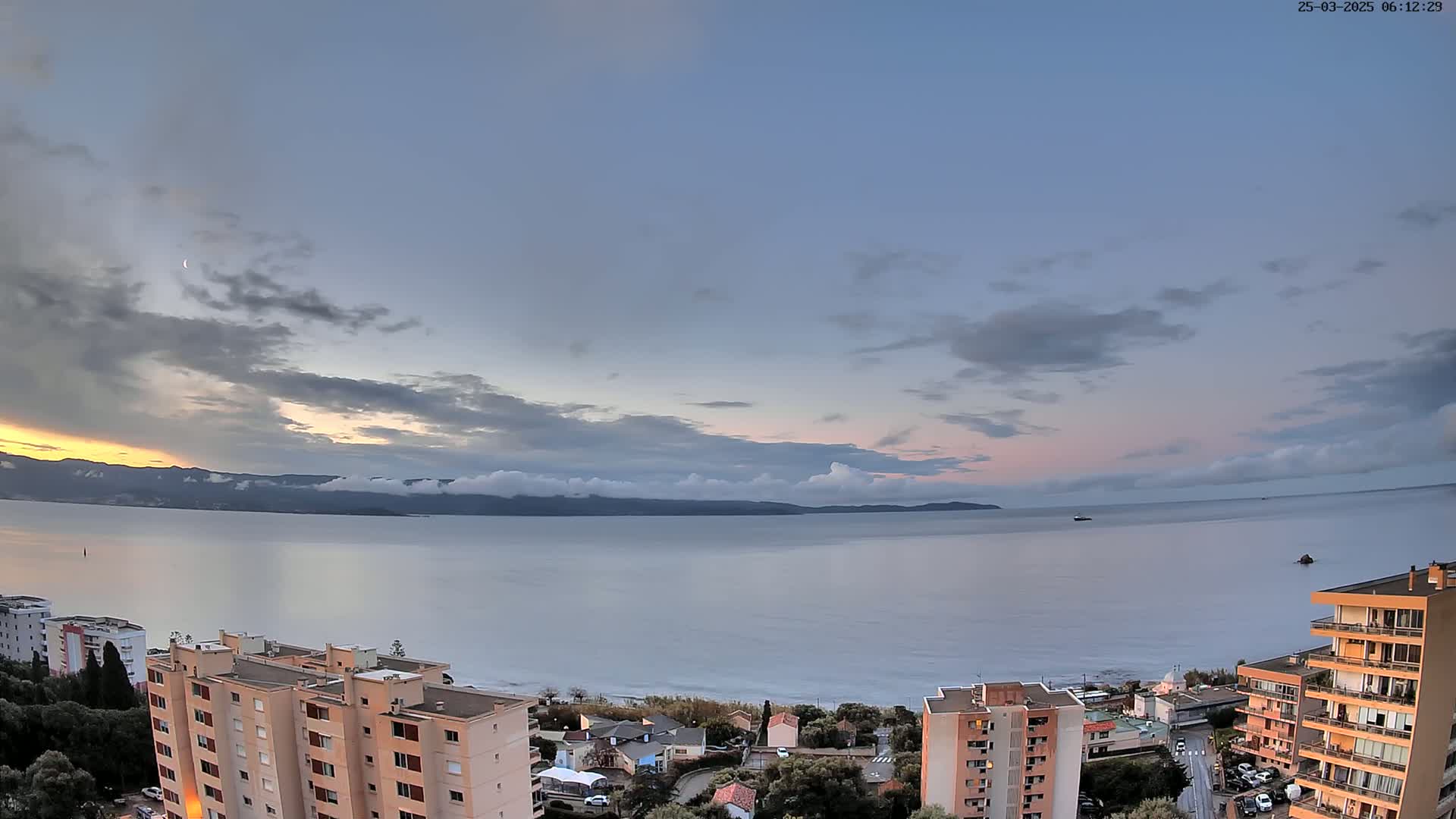 A calm body of water stretches to a distant mountain range under a partly cloudy, pale twilight sky.