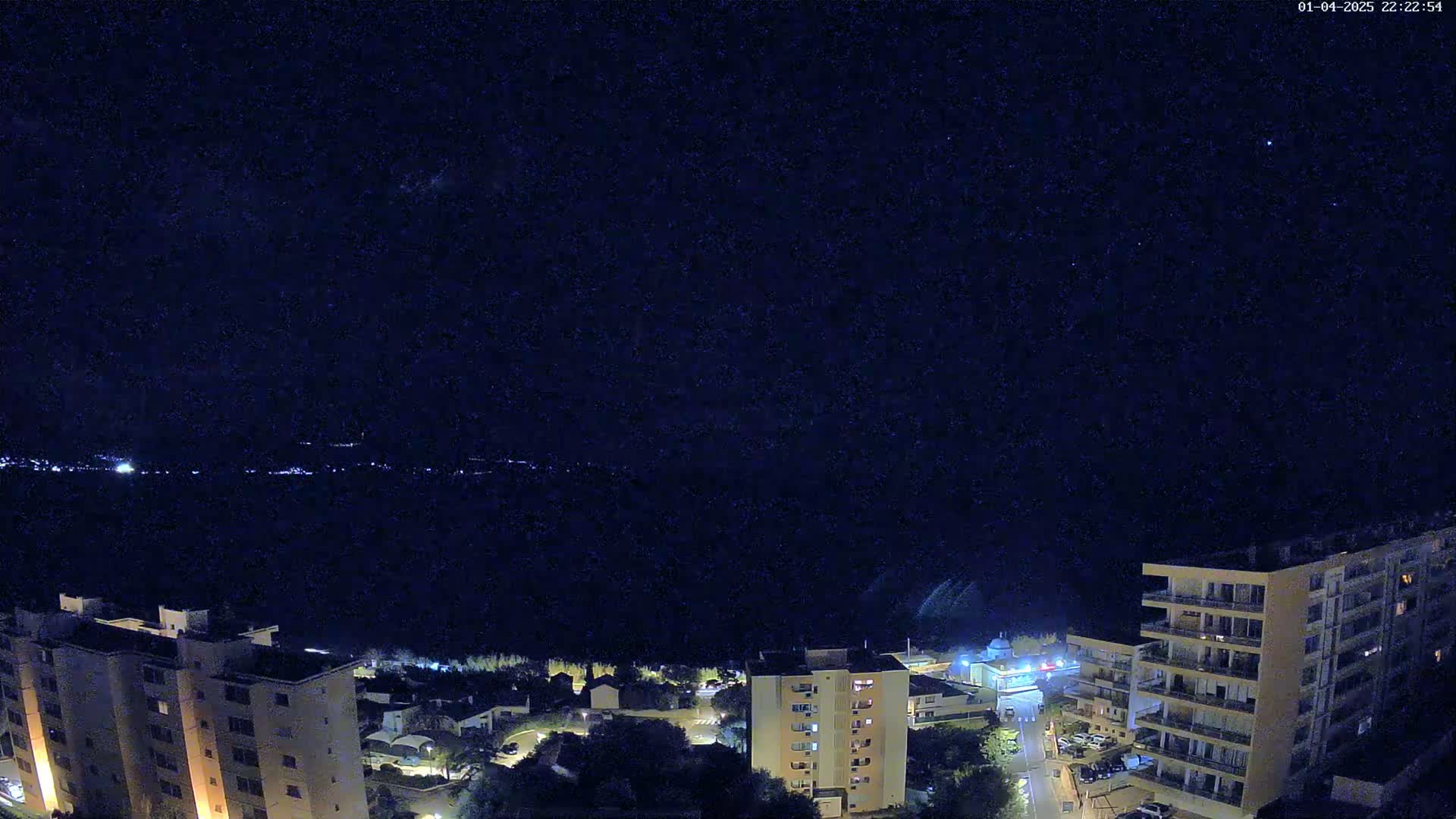 A nighttime, high-angle view shows a city with several multi-story buildings illuminated against a dark, starry sky.