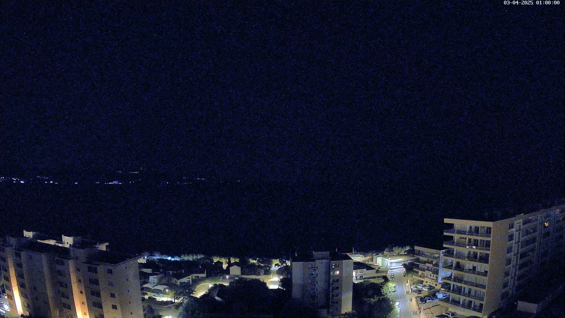 A nighttime, high-angle view shows several apartment buildings illuminated against a dark sky.