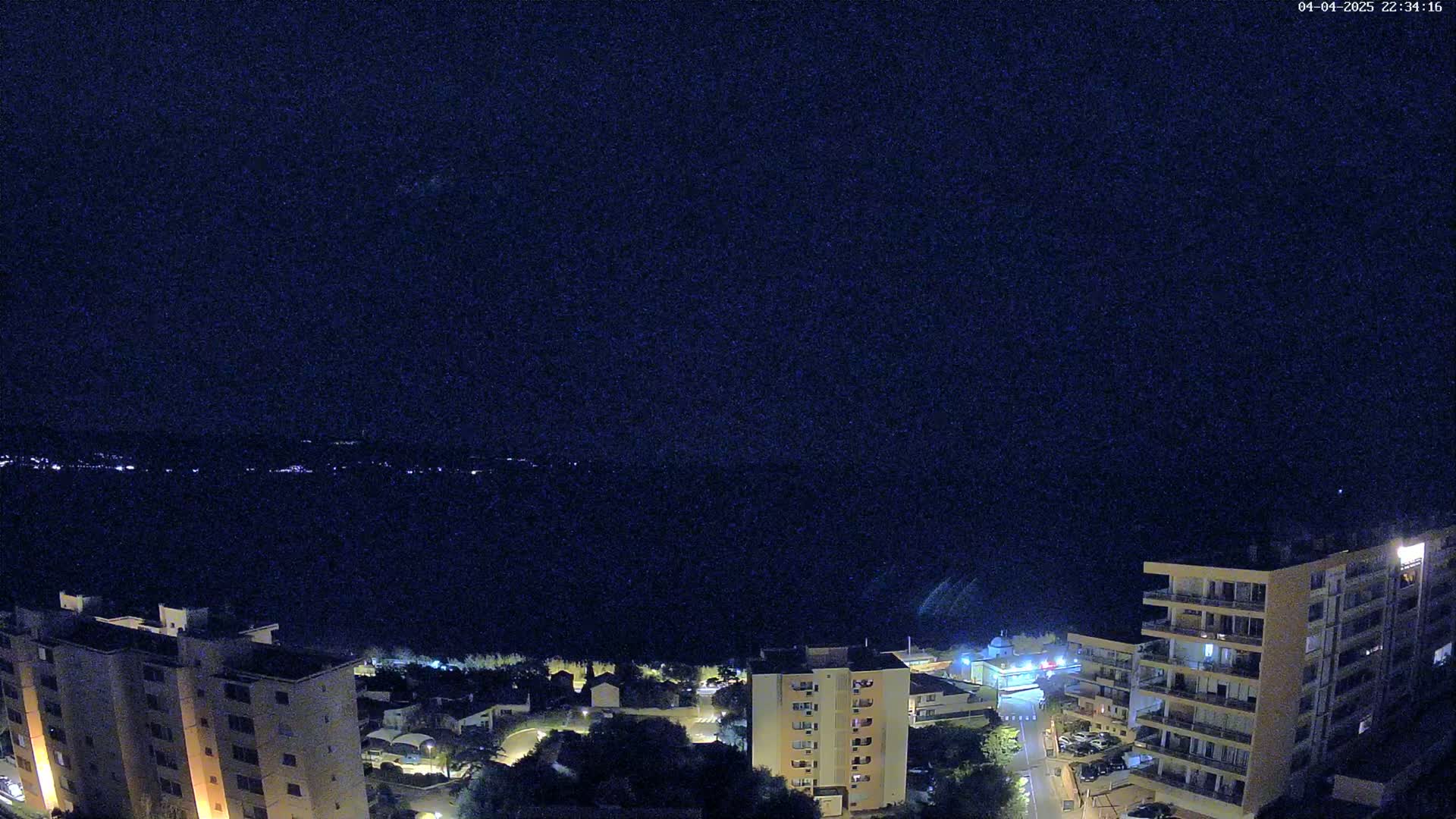 A nighttime view of apartment buildings overlooking a dark body of water under a clear sky.