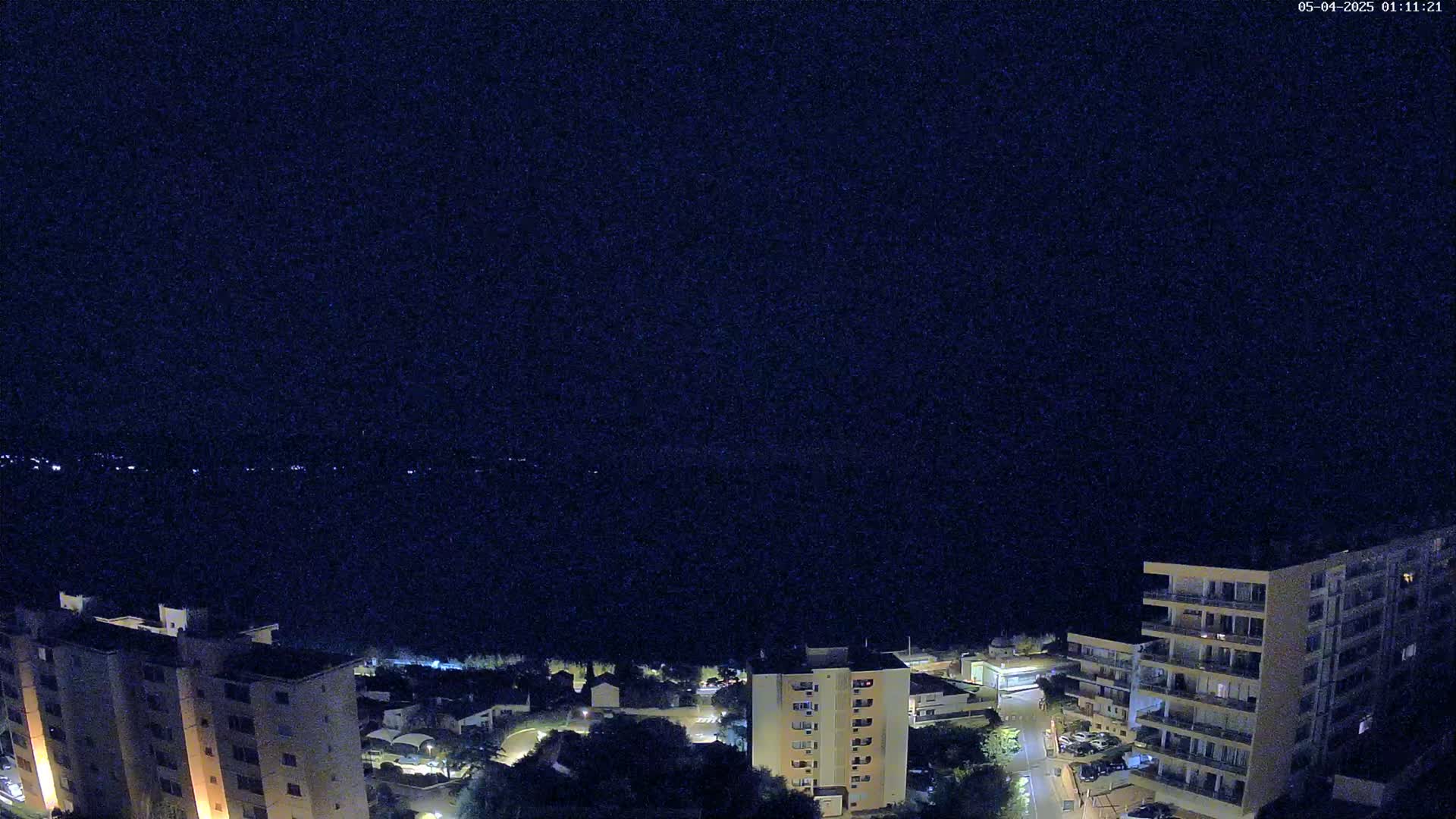 A nighttime view of apartment buildings and a small town overlooking a dark body of water under a clear sky.