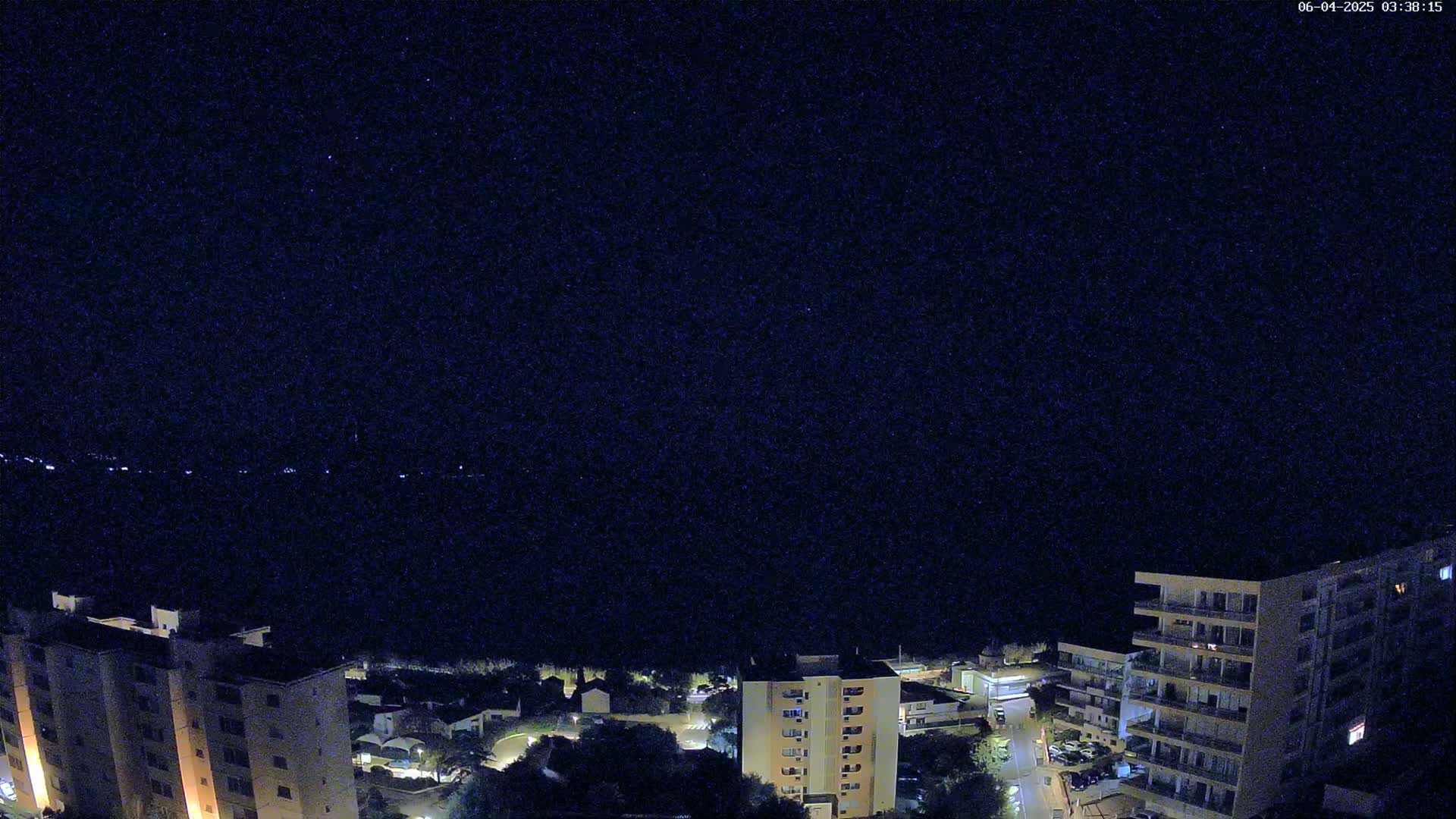 A nighttime, high-angle view shows a dark body of water below several illuminated apartment buildings.
