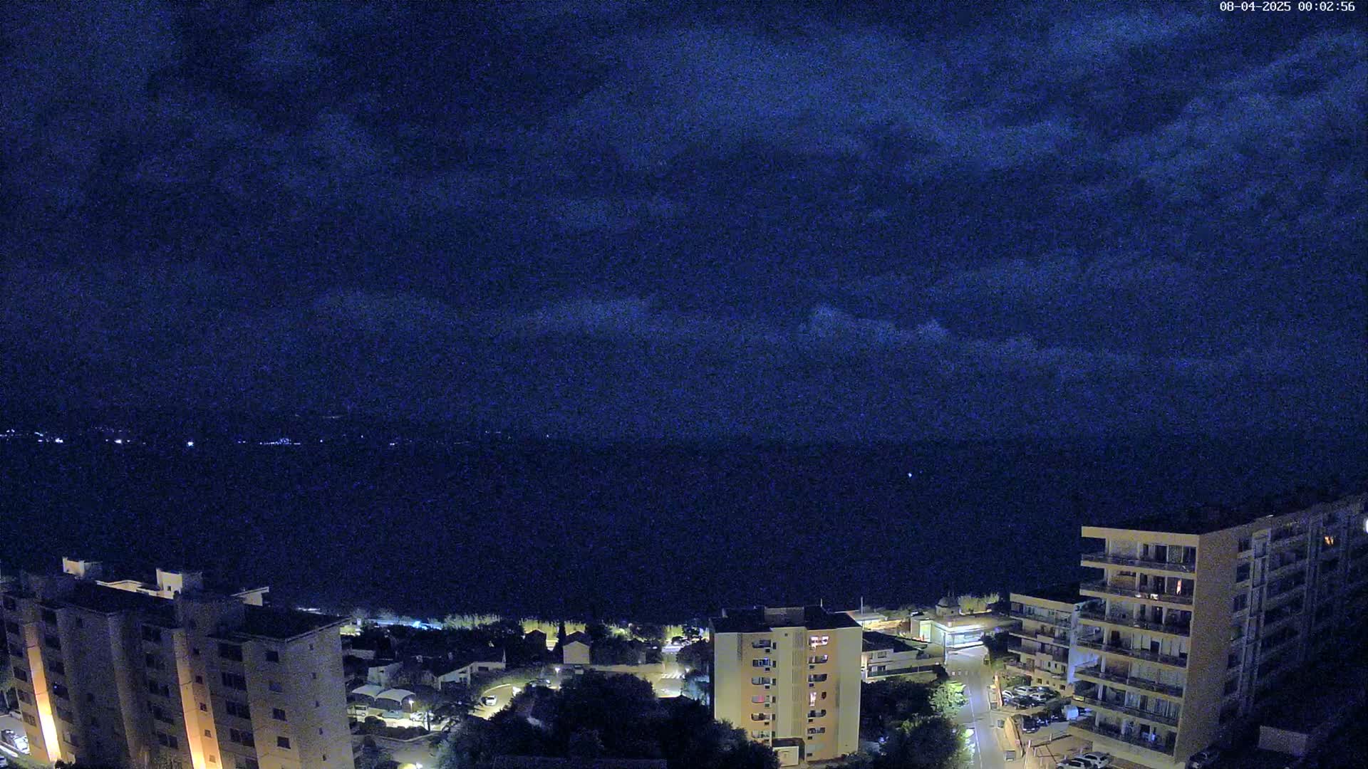 A nighttime view of apartment buildings overlooking a dark body of water under a cloudy sky.