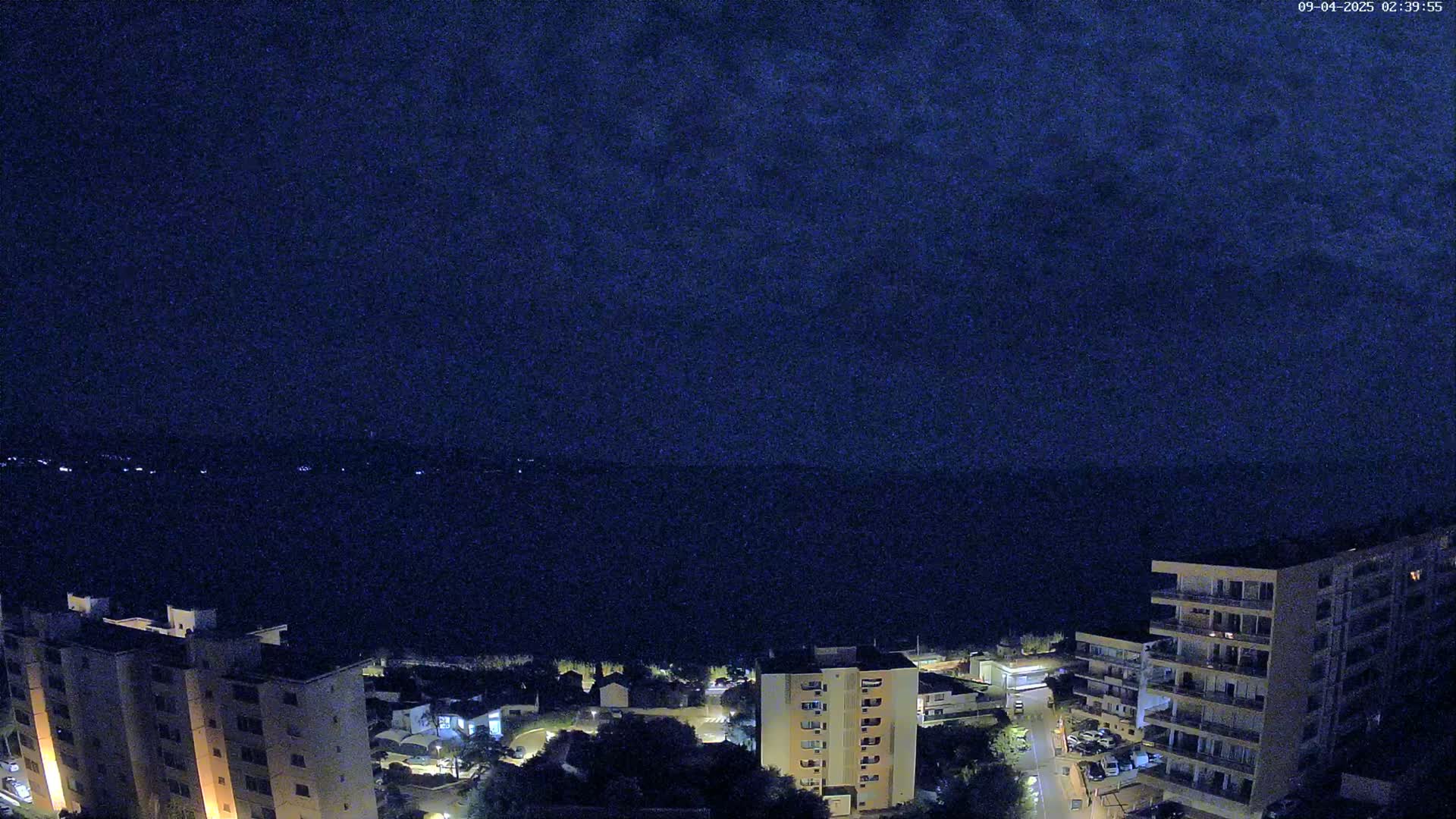 A nighttime, high-angle view shows several apartment buildings illuminated against a dark, cloudy sky.