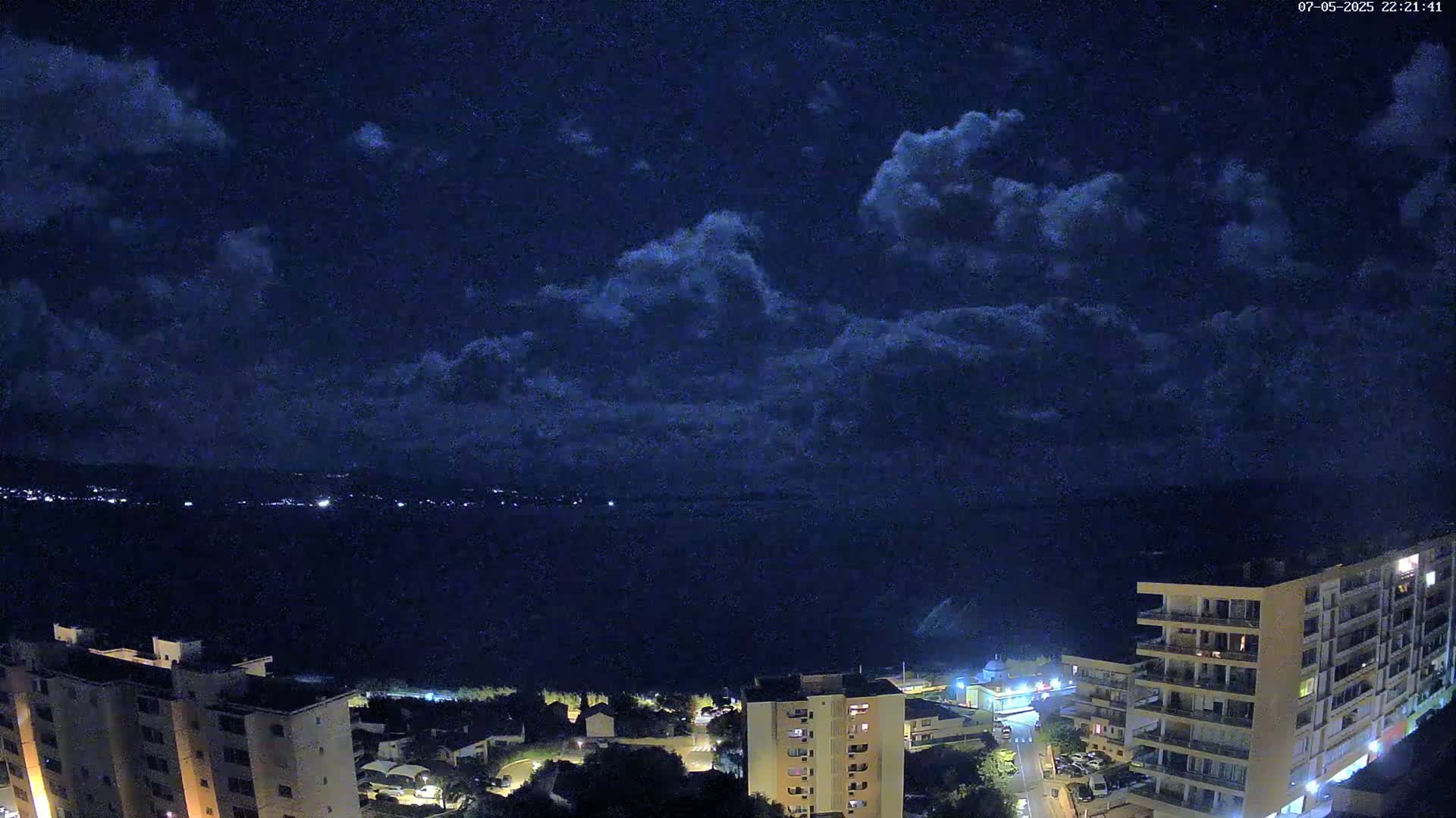 A nighttime view of a city overlooking a dark body of water under a cloudy sky.