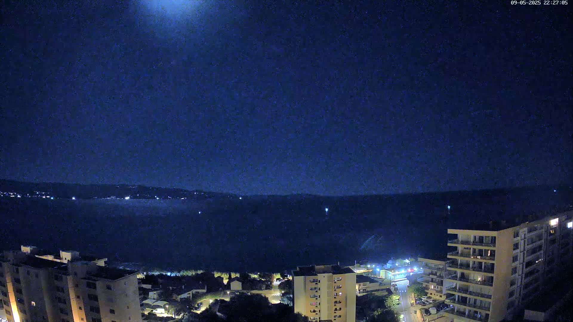 A nighttime, clear view of a body of water with a distant shoreline and several buildings illuminated, under a dark, starry sky.