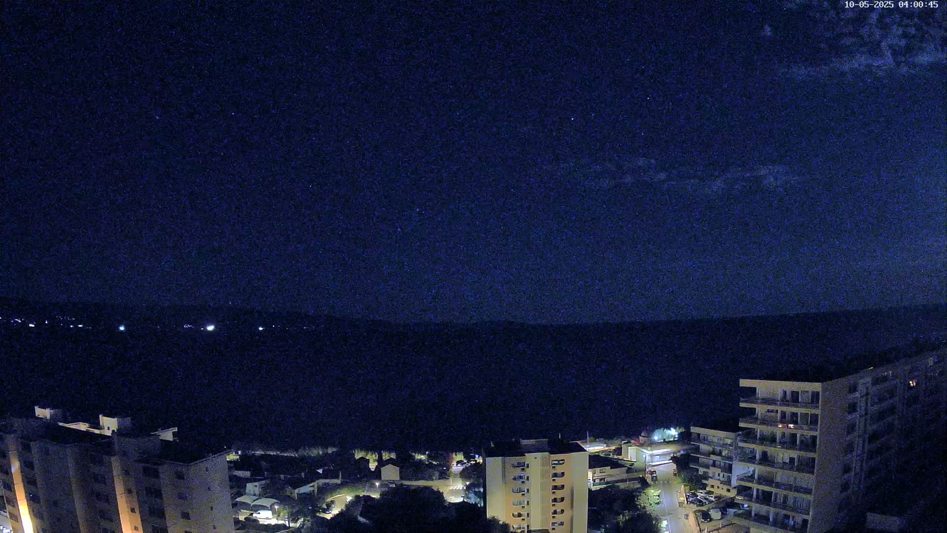 A nighttime aerial view shows a cityscape of multi-story buildings under a clear, dark, starry sky.