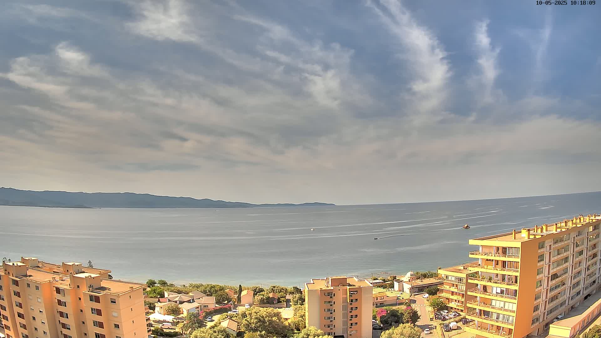 A partly cloudy sky overlooks a calm sea, a beach, and several apartment buildings.