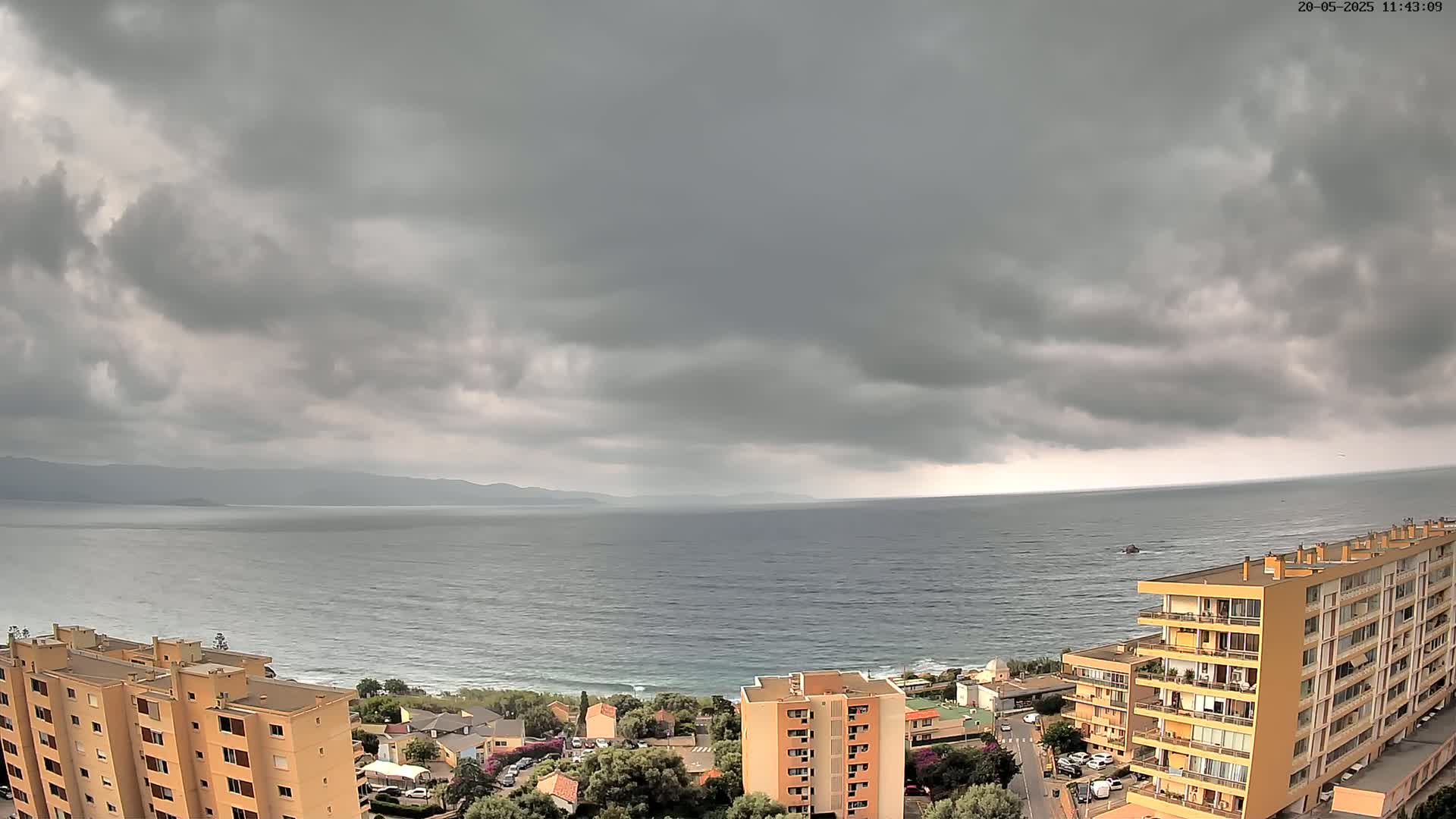 An overcast sky hangs over a calm sea, with several multi-story buildings and a town visible in the foreground.
