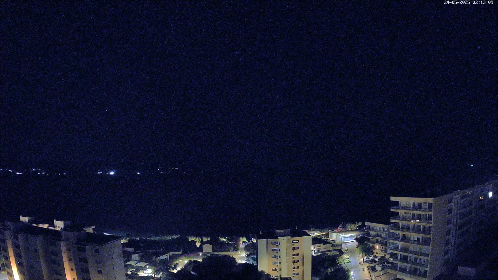 A nighttime, starlit view overlooking a coastal town with several multi-story buildings.