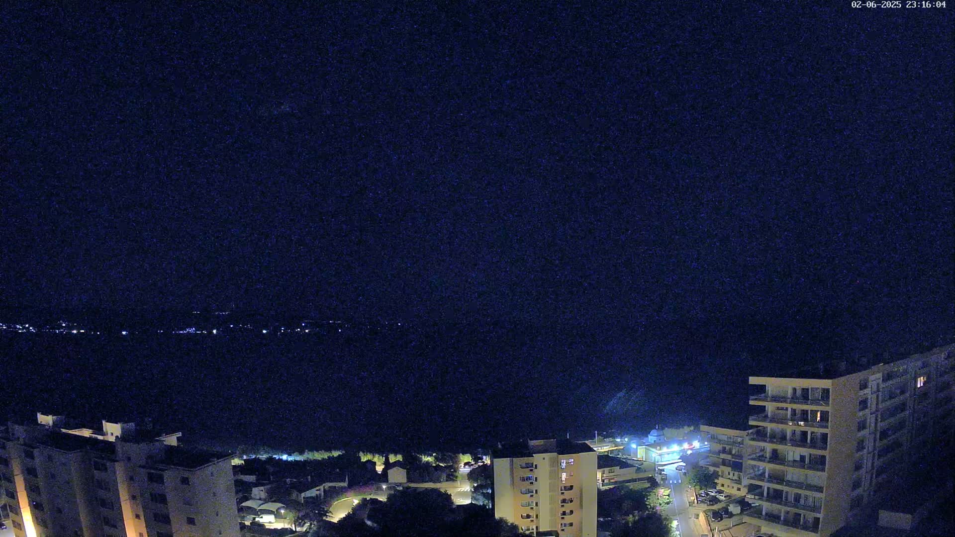 A nighttime view of a coastal town shows multi-story buildings under a clear, dark sky.
