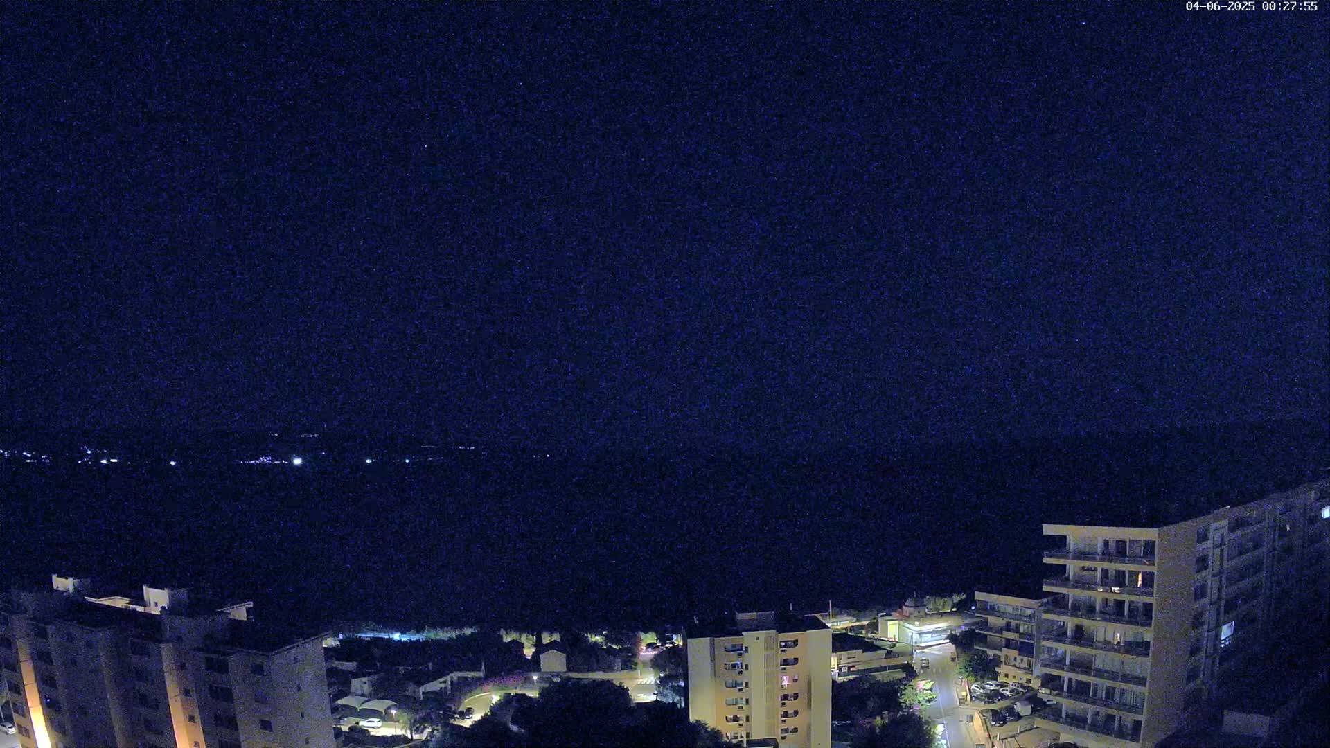 A nighttime, high-angle view shows several multi-story buildings illuminated against a dark sky over a body of water.
