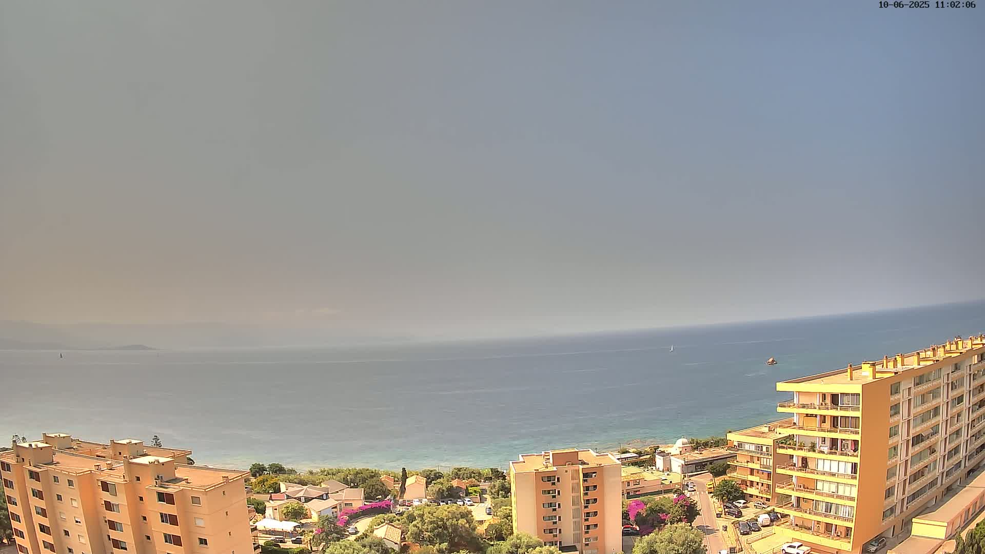 A hazy, sunny day overlooks a calm sea from a high vantage point showing apartment buildings and a small coastal town.