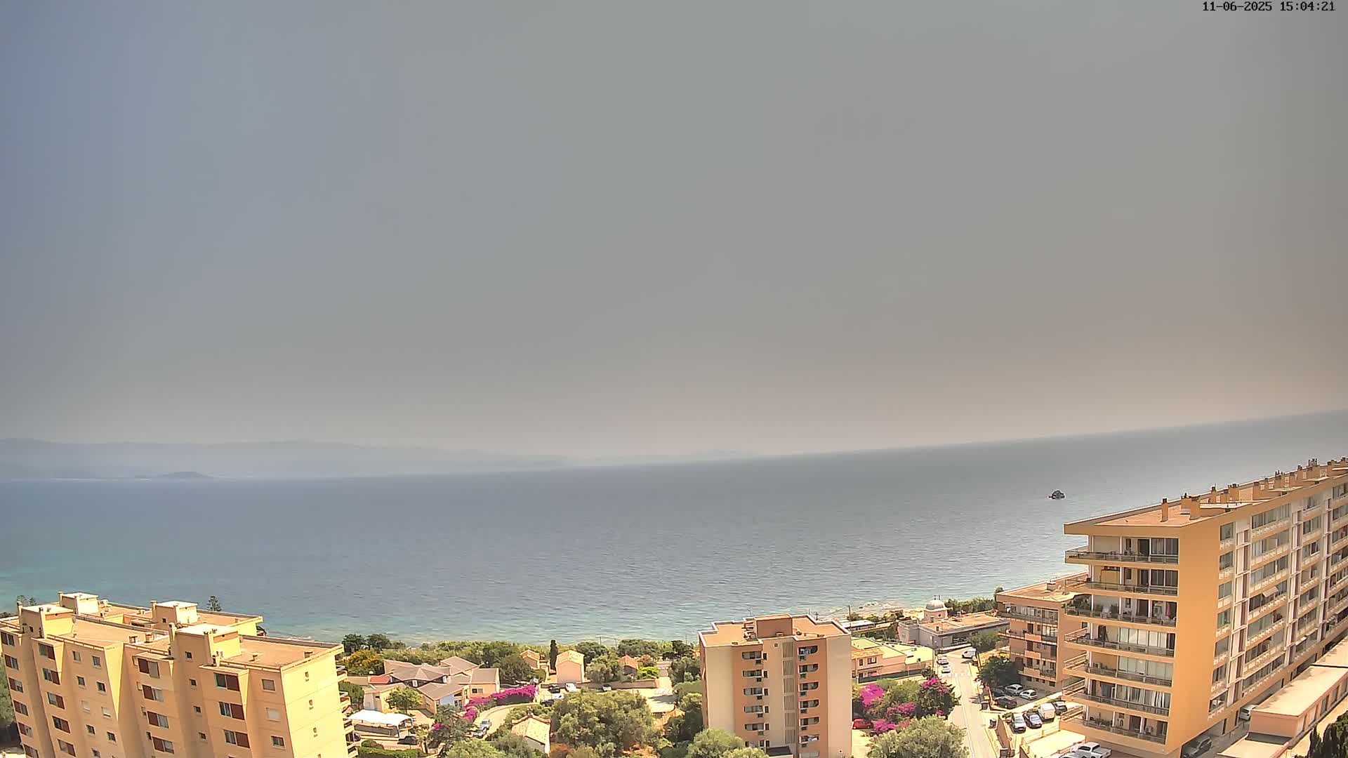 A hazy, sunny day overlooking a calm sea and coastal buildings from an elevated vantage point.