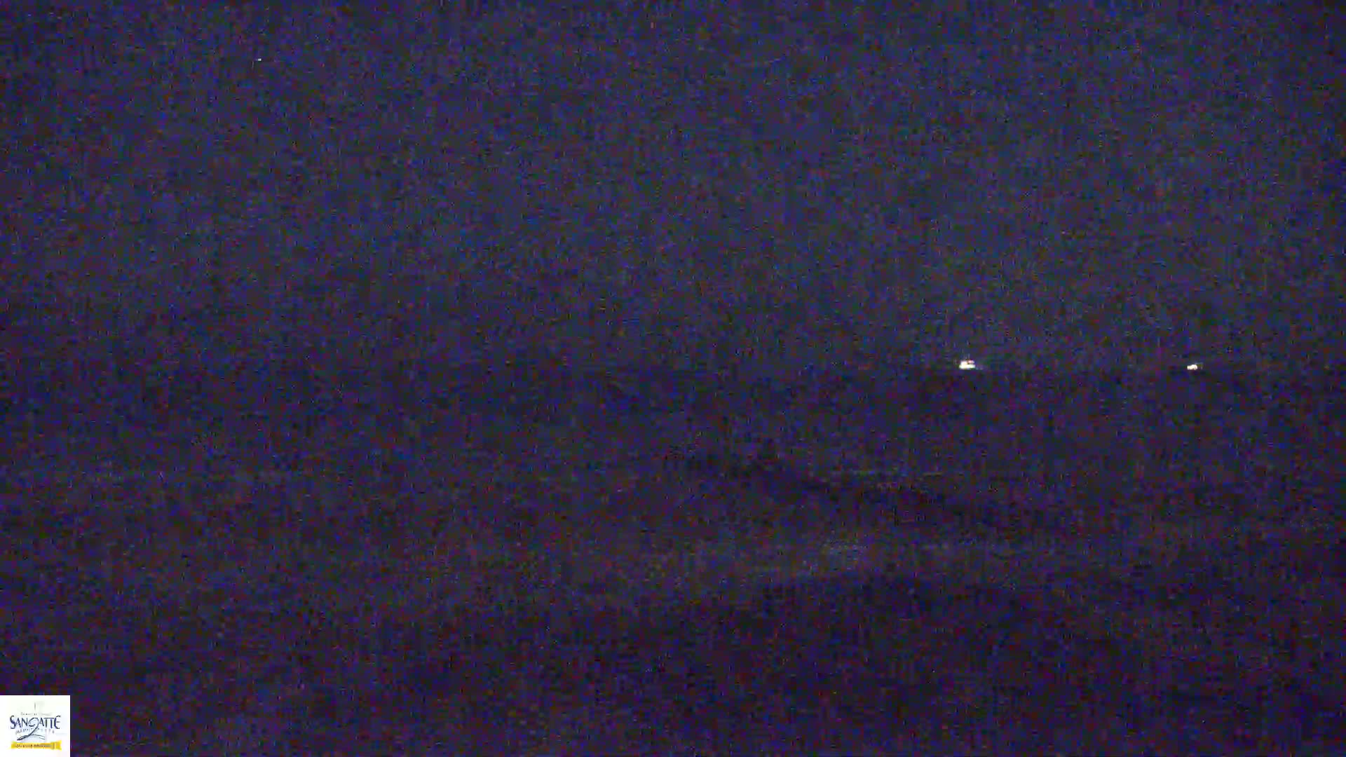 A dark, nighttime scene shows a distant horizon with two faint lights visible under a dark sky.