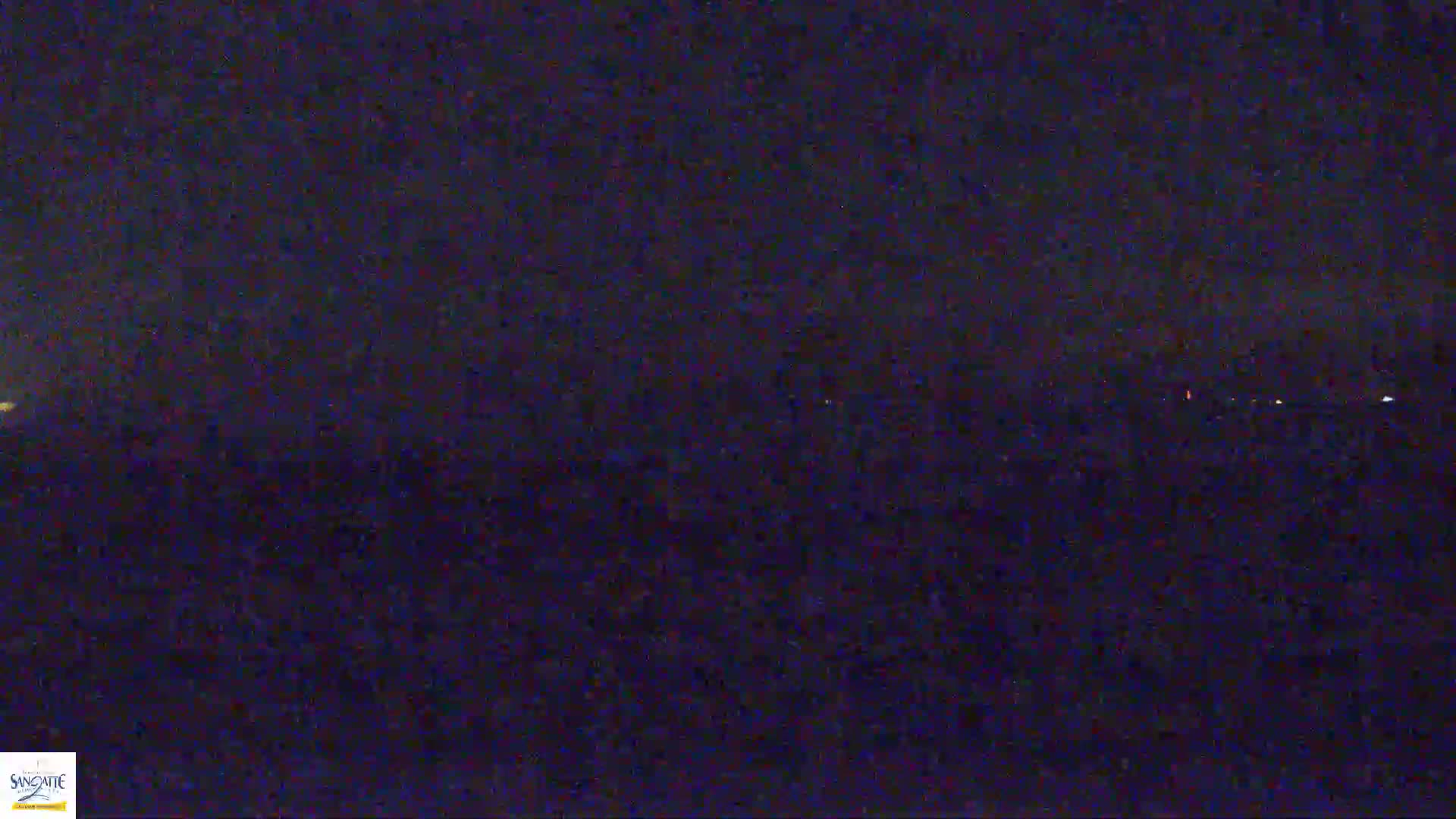 A dark, nighttime view shows a distant horizon with faint lights, under a mostly clear sky.