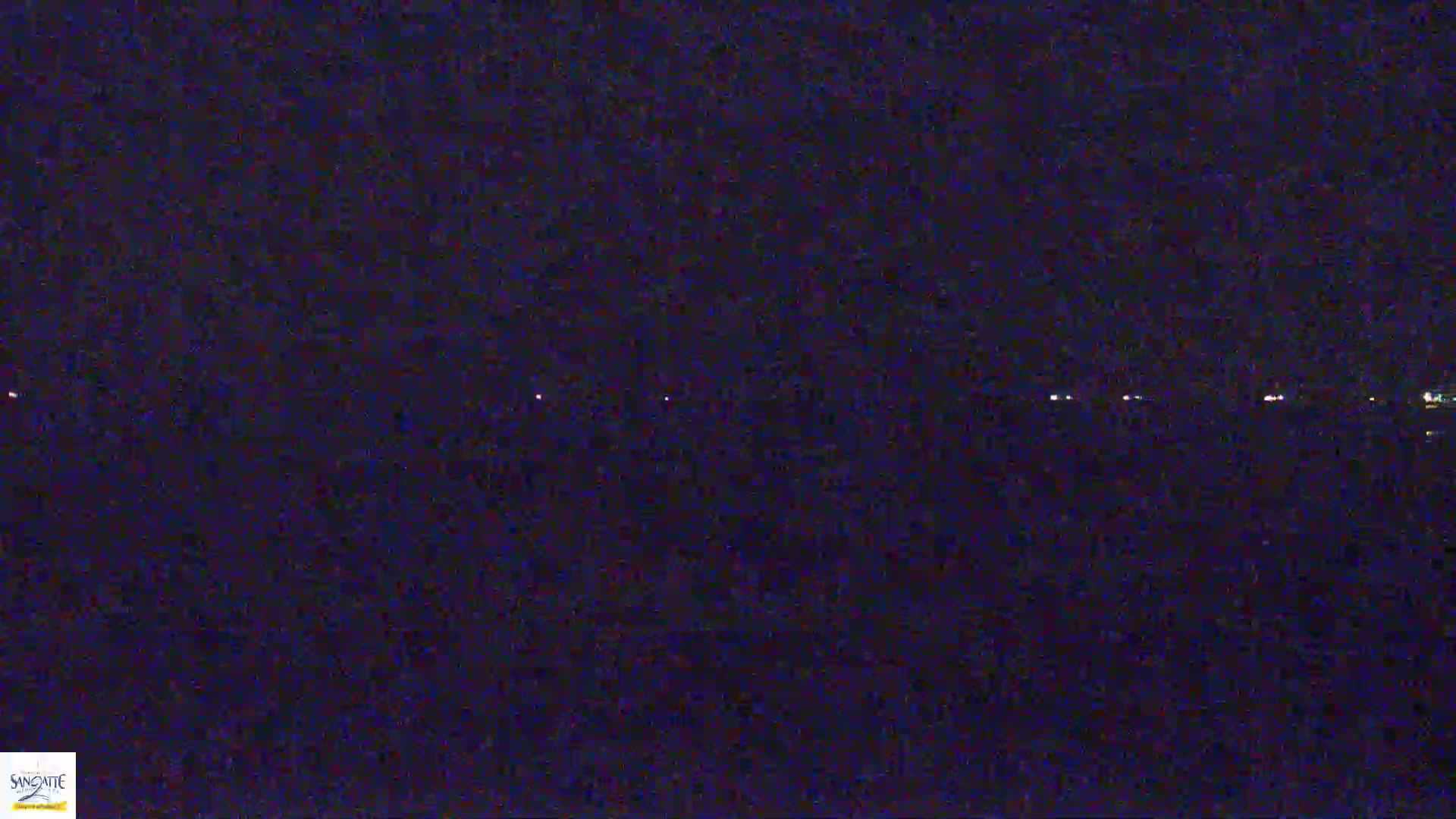 A dark, nighttime scene shows a distant line of faint lights on the horizon.