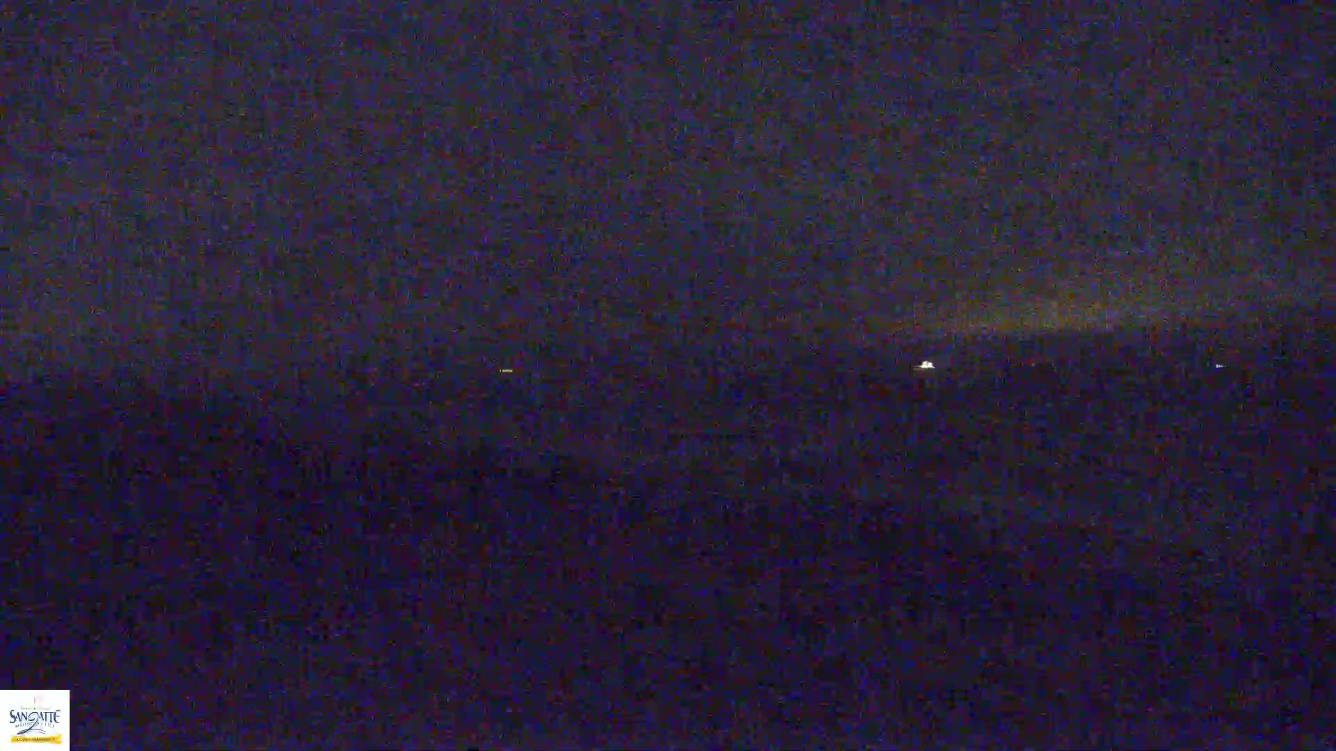 A dark, nighttime scene shows a few distant lights on a dark body of water under a mostly clear sky.
