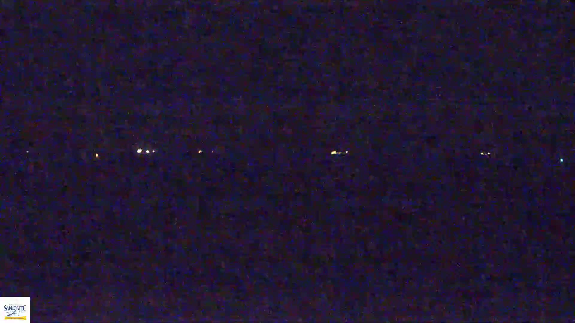 A dark, nighttime scene shows a line of distant, faint lights across a dark horizon.