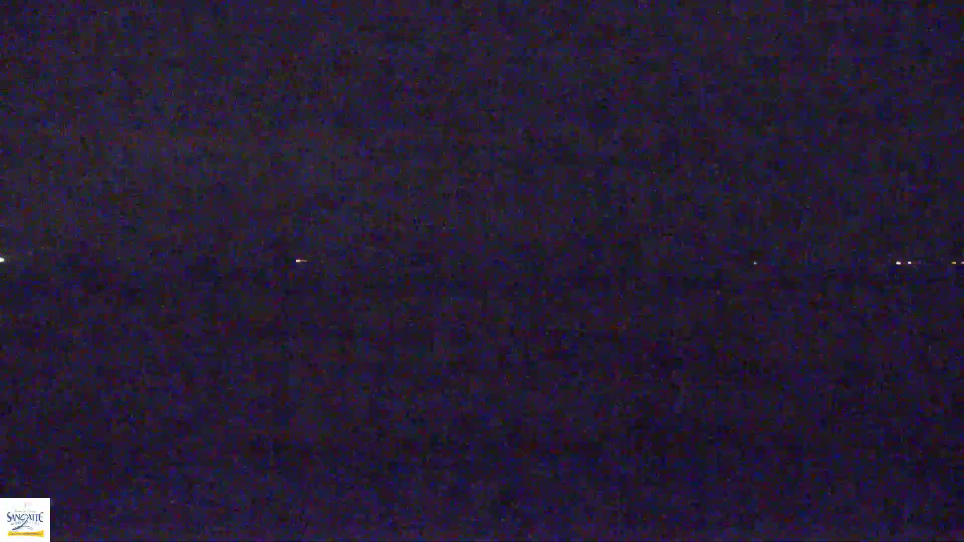 A dark, nighttime scene shows a line of distant lights on a dark body of water under a clear, starless sky.
