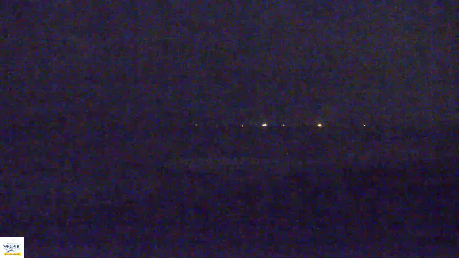 A dark, nighttime scene shows a distant line of faint lights on the horizon.