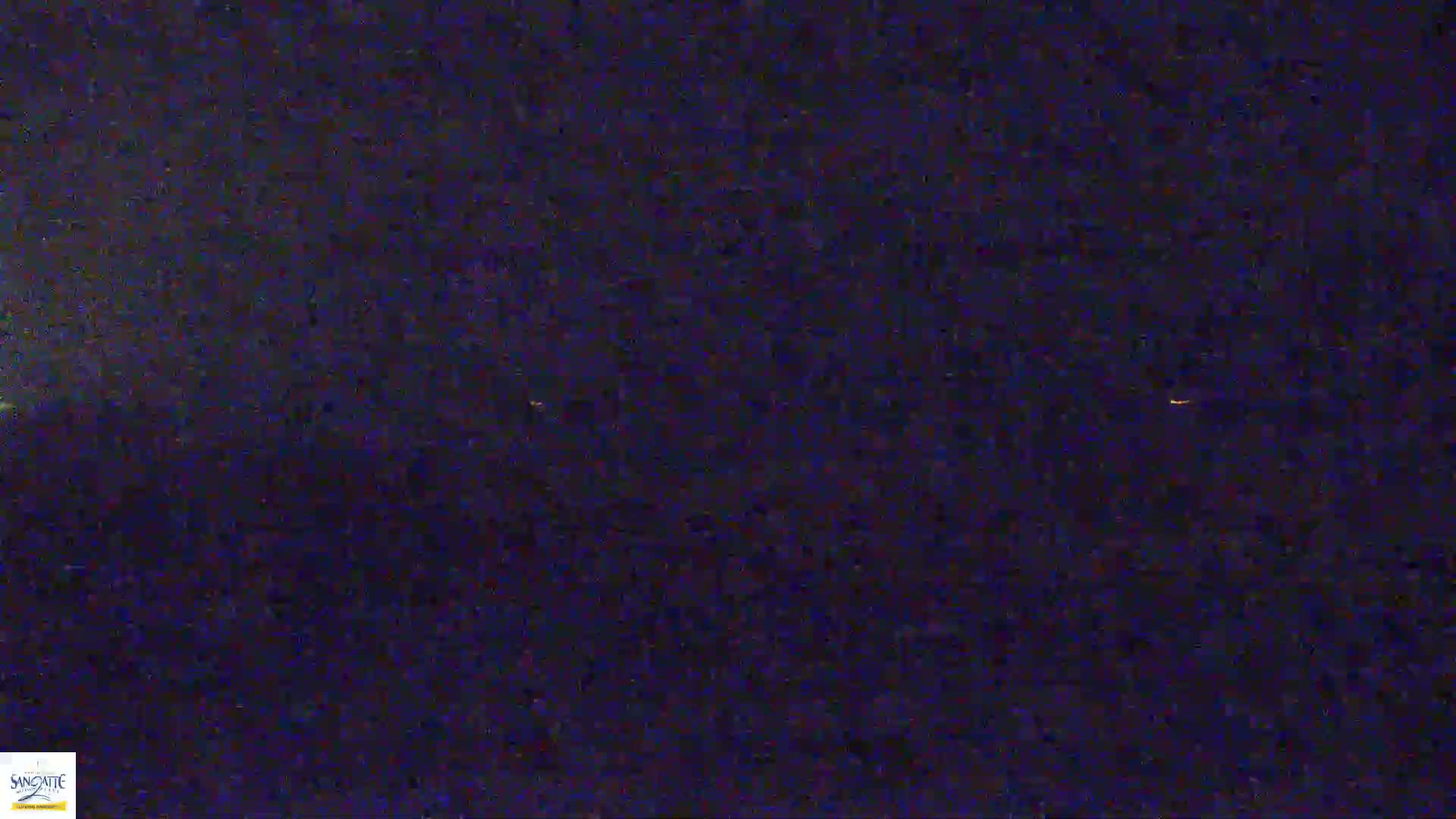 A nighttime, low-light view shows a dark landscape with a few faint, distant lights visible on the horizon.