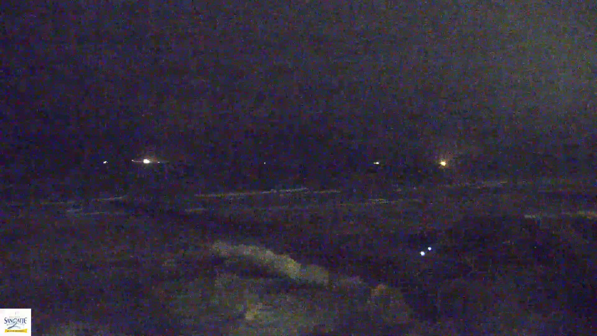 A nighttime, low-light view of a dark ocean with small waves and a few distant lights on the horizon.