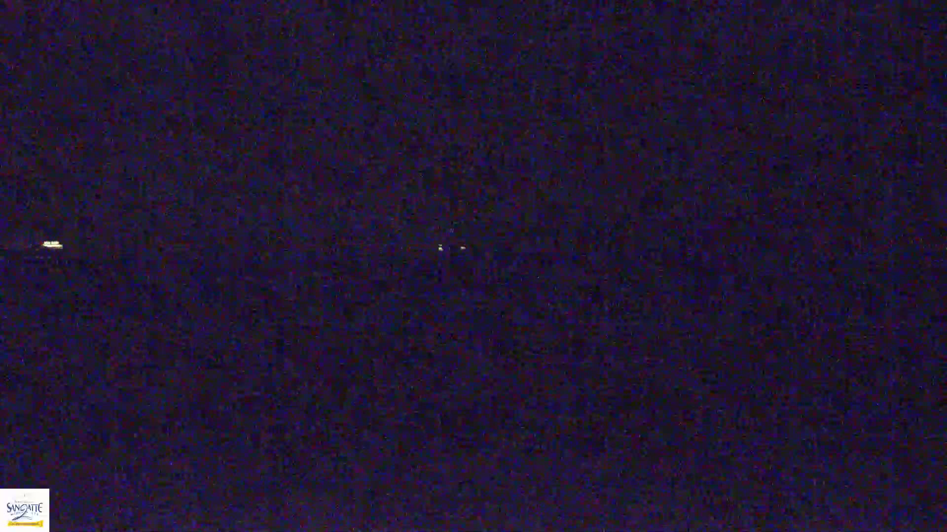A dark, nighttime scene shows a few distant, faint lights in a mostly uniform, dark expanse.