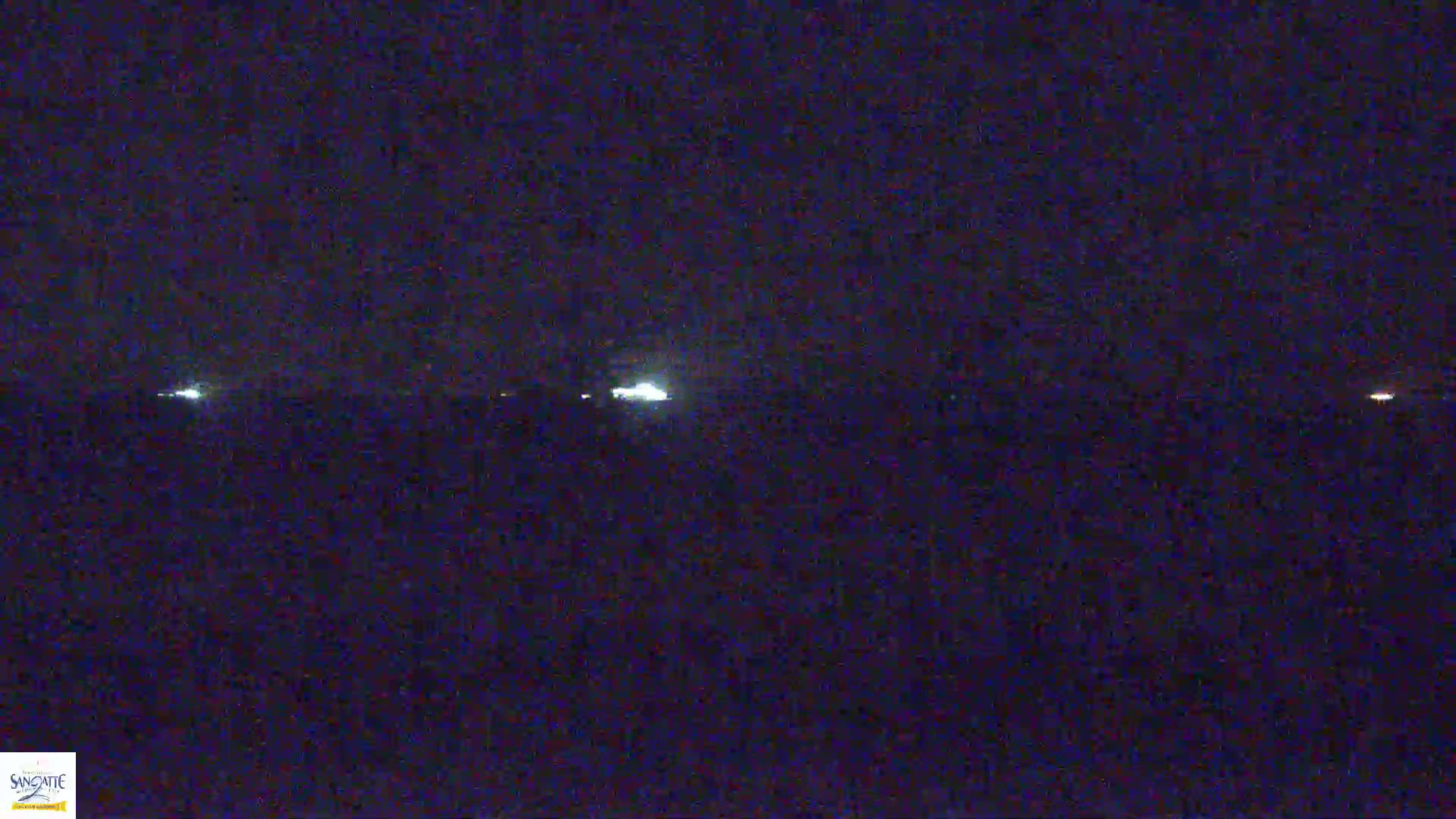 A dark, nighttime scene shows several faint, distant lights on a flat horizon under a clear, dark sky.